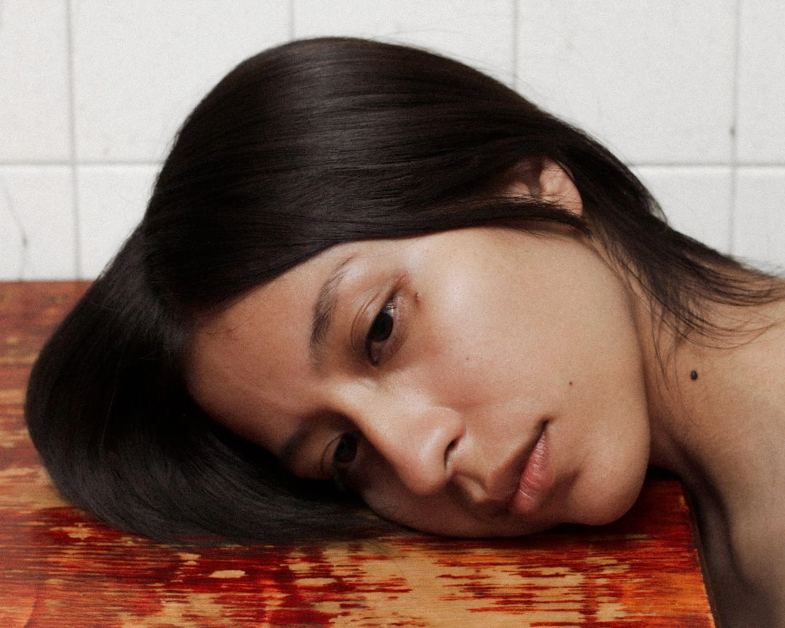 Bravo by Felipe Romero Beltrán — A portrait of a subject resting their head on a rendered wall surface painted in two distinct sections—terracotta-red below, slate-grey above.