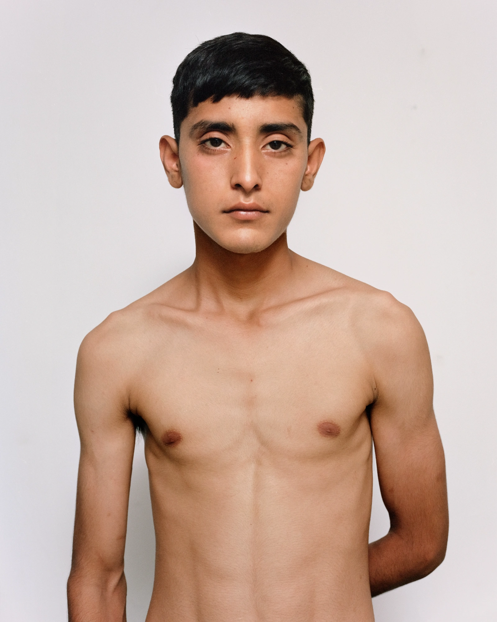Bravo by Felipe Romero Beltrán — A frontal portrait of a young man positioned against a two-tone wall divided by a sharp vertical line: terracotta-red render on the left, slate-grey on the...