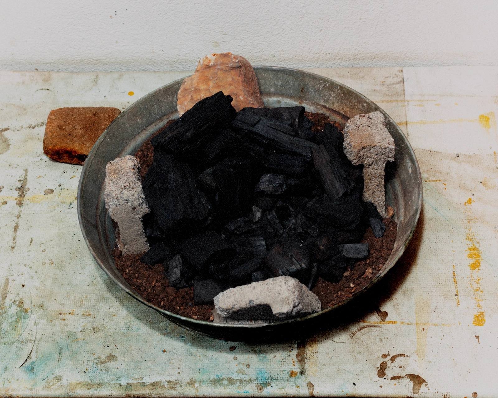 Bravo by Felipe Romero Beltrán — A metal basin sits on a weathered concrete floor, its surface filled with charred wood fragments and ash.