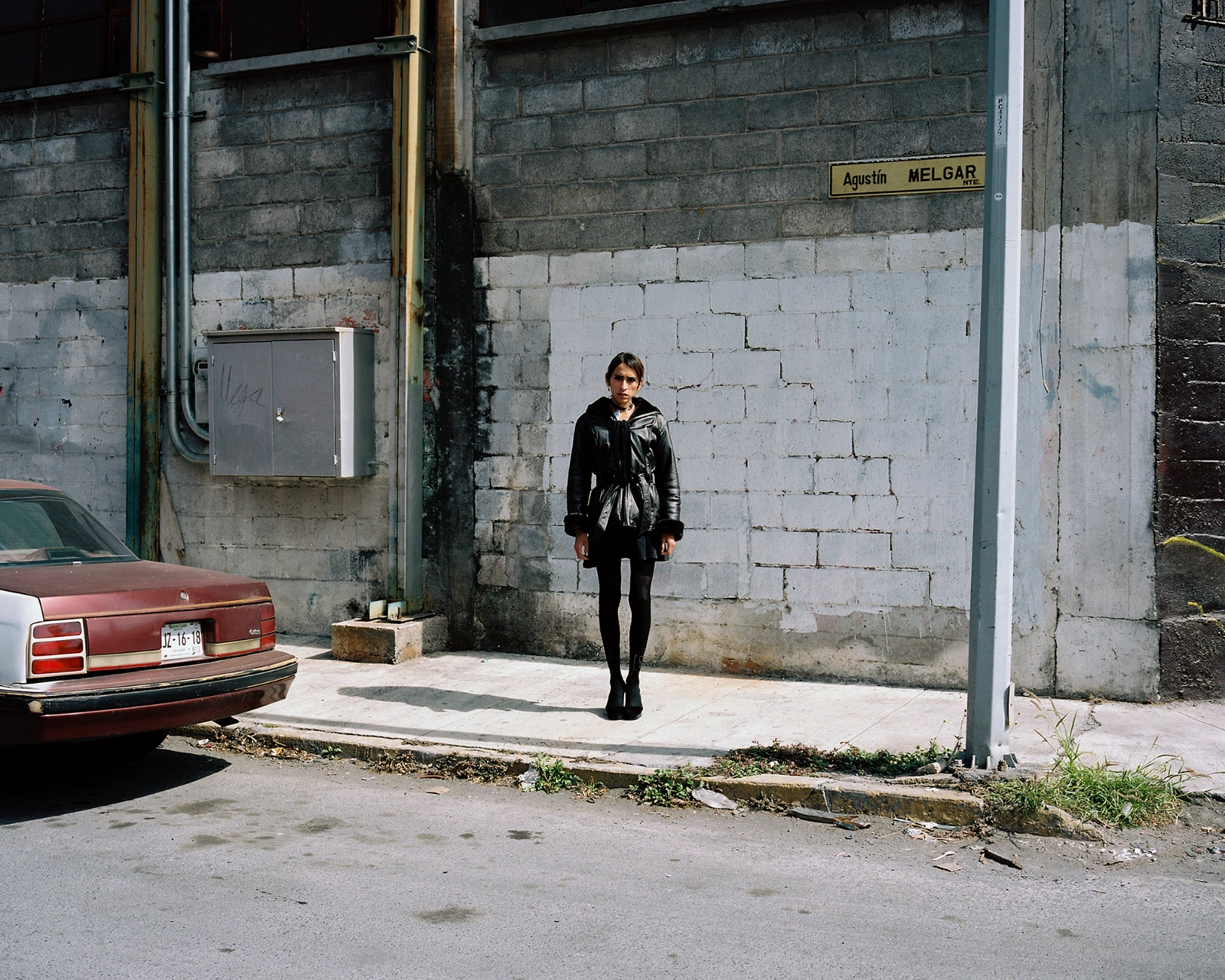 Bravo by Felipe Romero Beltrán — A figure in black leather jacket and sunglasses stands centered before a two-tone concrete wall on Agustín Melgar street in Rio Bravo.