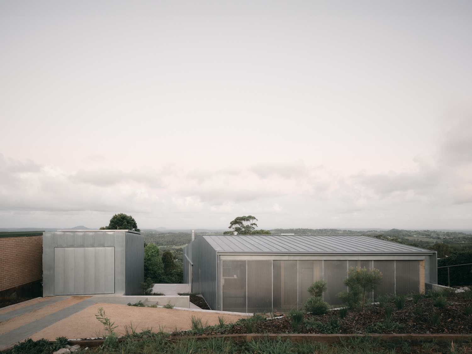 Mapleton House by Atelier Chen Hung — The corrugated metal facade and pitched roof of the eastern elevation frame the landscaped approach to Mapleton House.