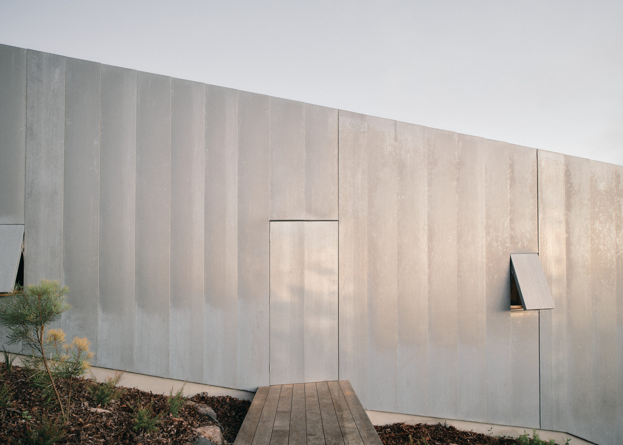 Mapleton House by Atelier Chen Hung — The rendered facade presents a monolithic composition of vertical panels in warm beige and cream tones, their subtle gradations revealing the texture of the...