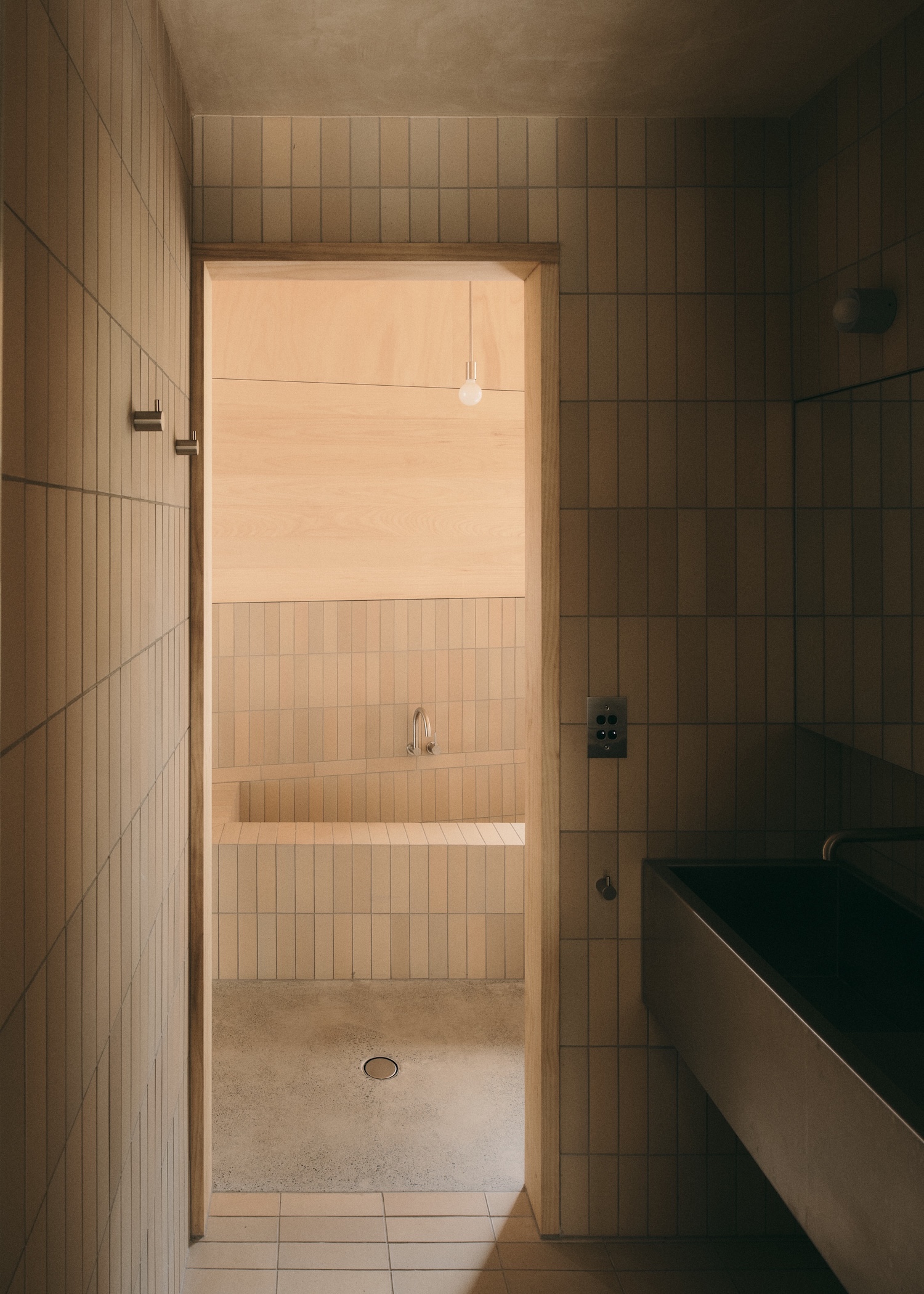 Mapleton House by Atelier Chen Hung — A passage views through to an open-plan bathing space defined by timber-lined walls in warm ochre tones.