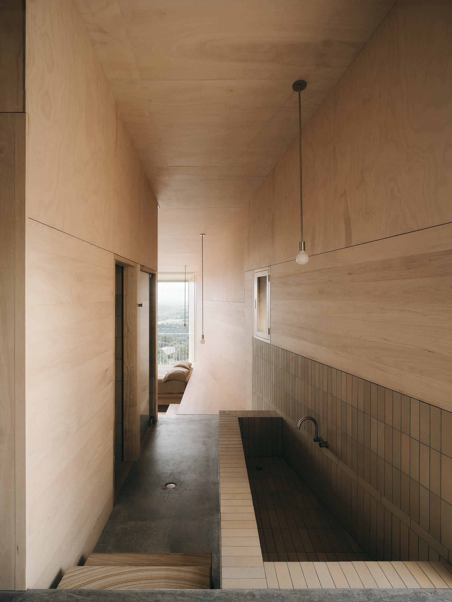 Mapleton House by Atelier Chen Hung — A narrow corridor lined with rammed-earth walls in warm ochre tones extends toward a framed mountain view.