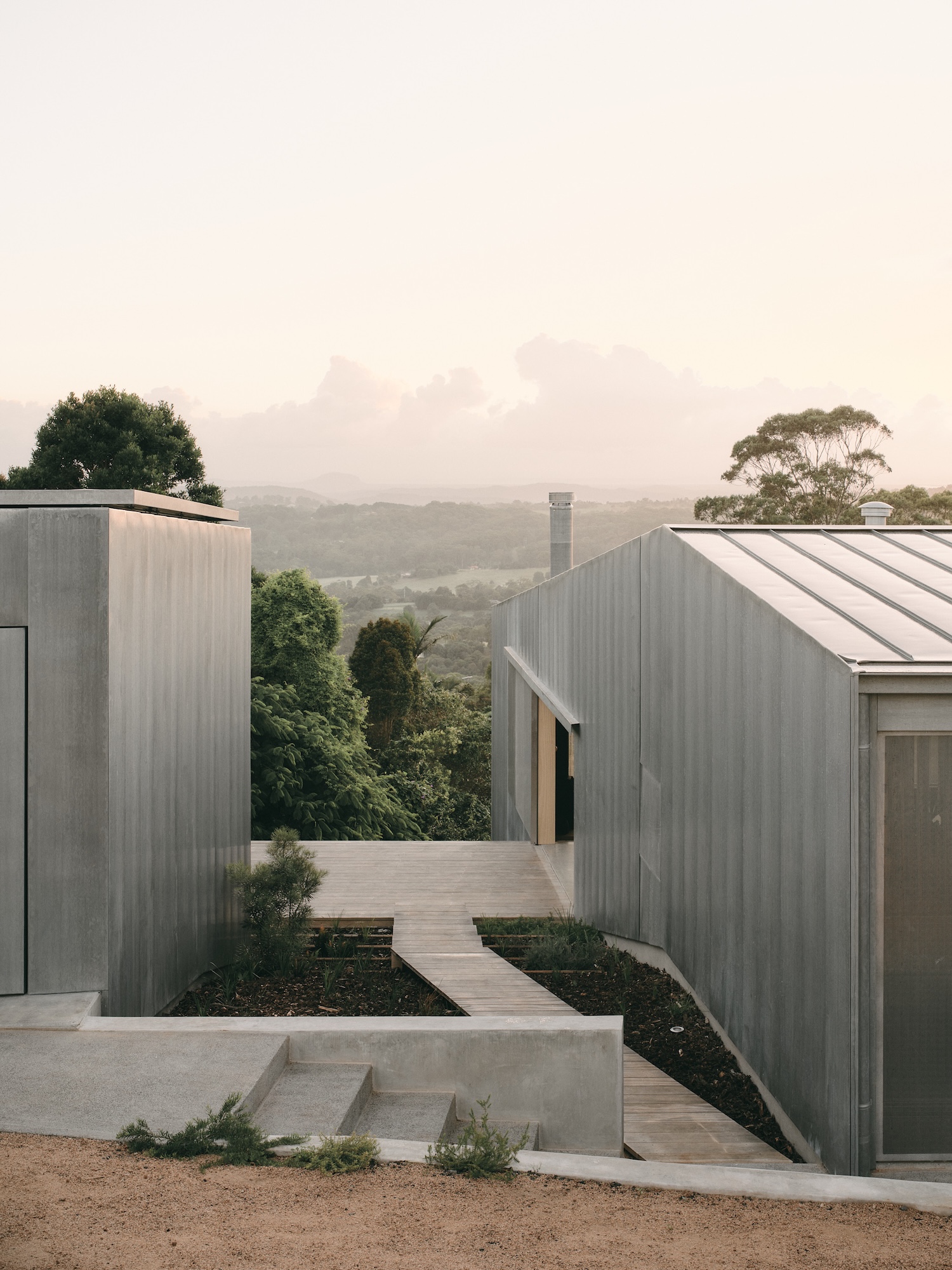 Mapleton House by Atelier Chen Hung — The passage between two corrugated metal pavilions frames the landscape beyond, with Mt.