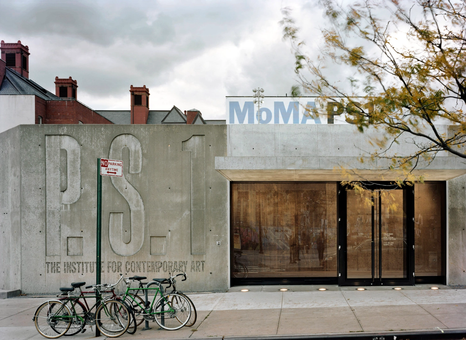 MoMA PS1 Entrance Building by Andrew Berman Architect — The entrance façade of MoMA PS1 presents a monolithic cast-concrete wall bearing deeply recessed numerals and institutional lettering, its surface marked by...