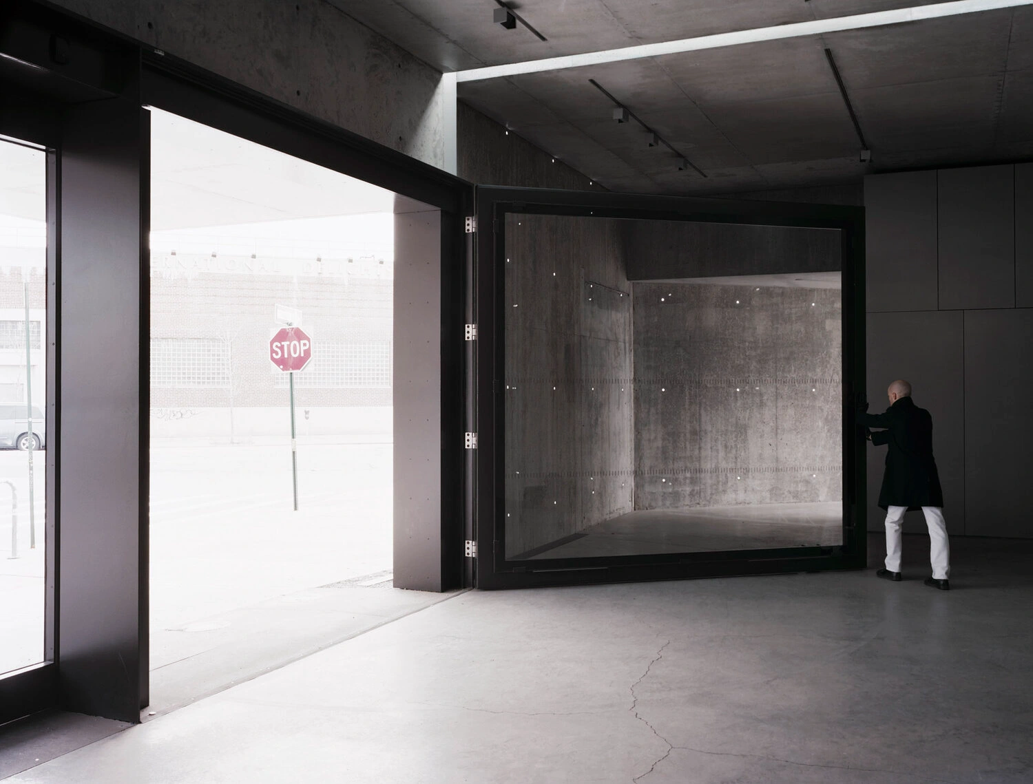 MoMA PS1 Entrance Building by Andrew Berman Architect — The entrance pavilion's interior threshold presents a volumetric concrete chamber with board-formed walls displaying visible formwork texture and weathering...