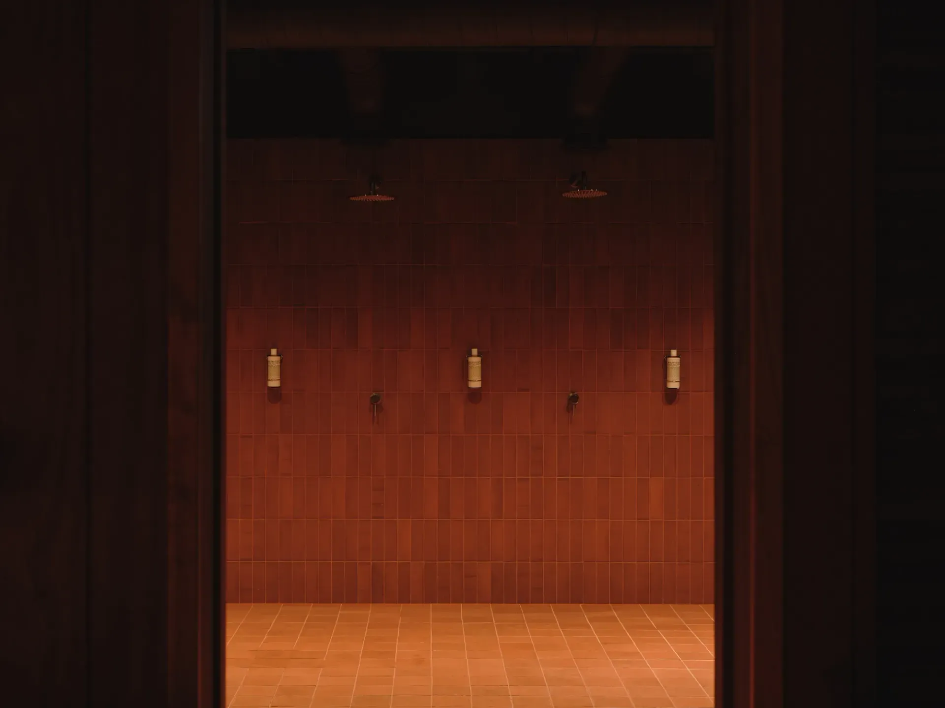 Arc Canary Wharf by Cake Architecture — A sauna interior viewed through a dark timber threshold, revealing terracotta floor tiles in a radial grid pattern ascending toward tiered bench seating.