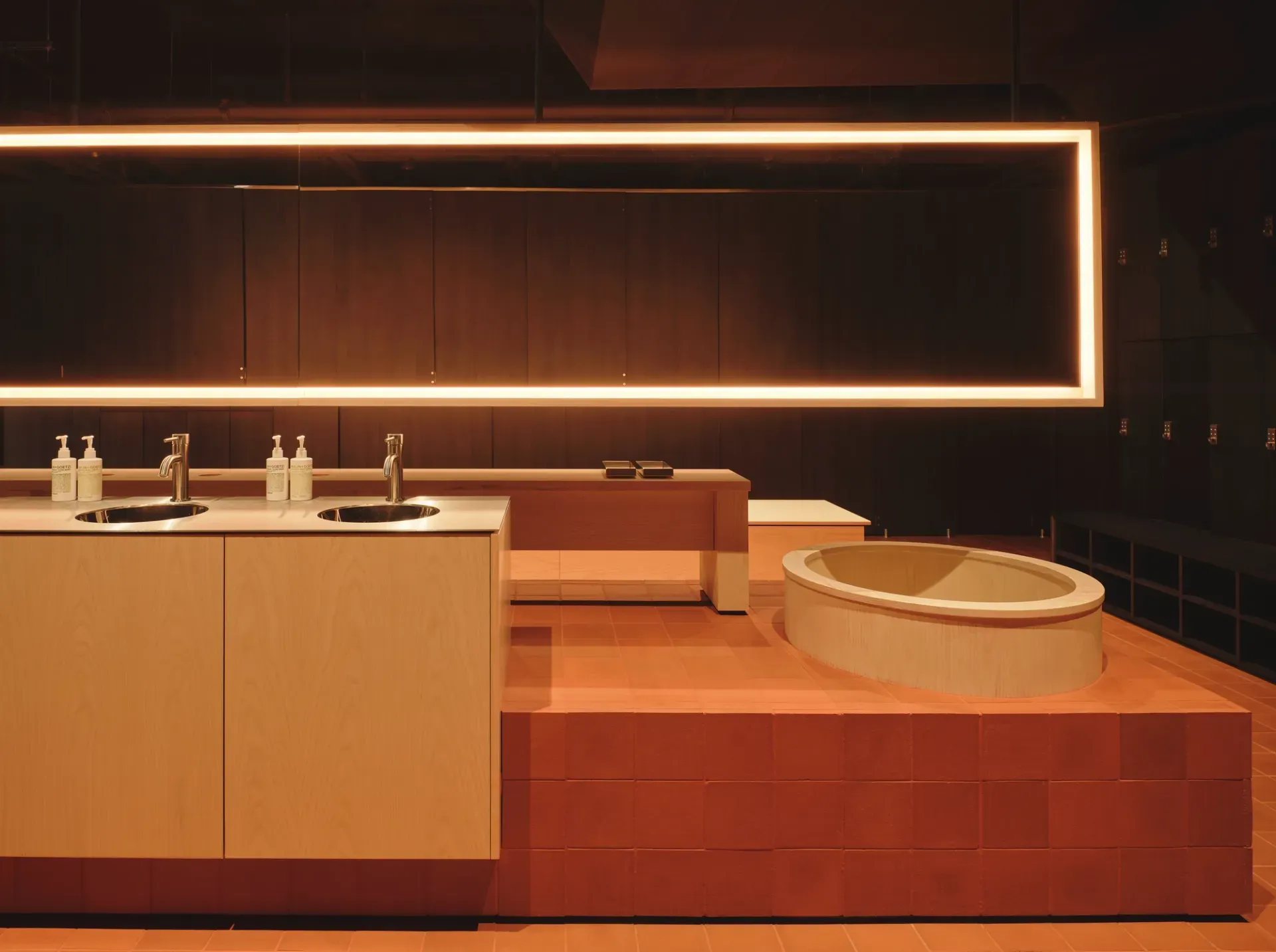 Arc Canary Wharf by Cake Architecture — The bathing area centres on a sculptural timber tub positioned on a stepped terracotta platform, its curved rim mirroring the concentric bench tiers that...