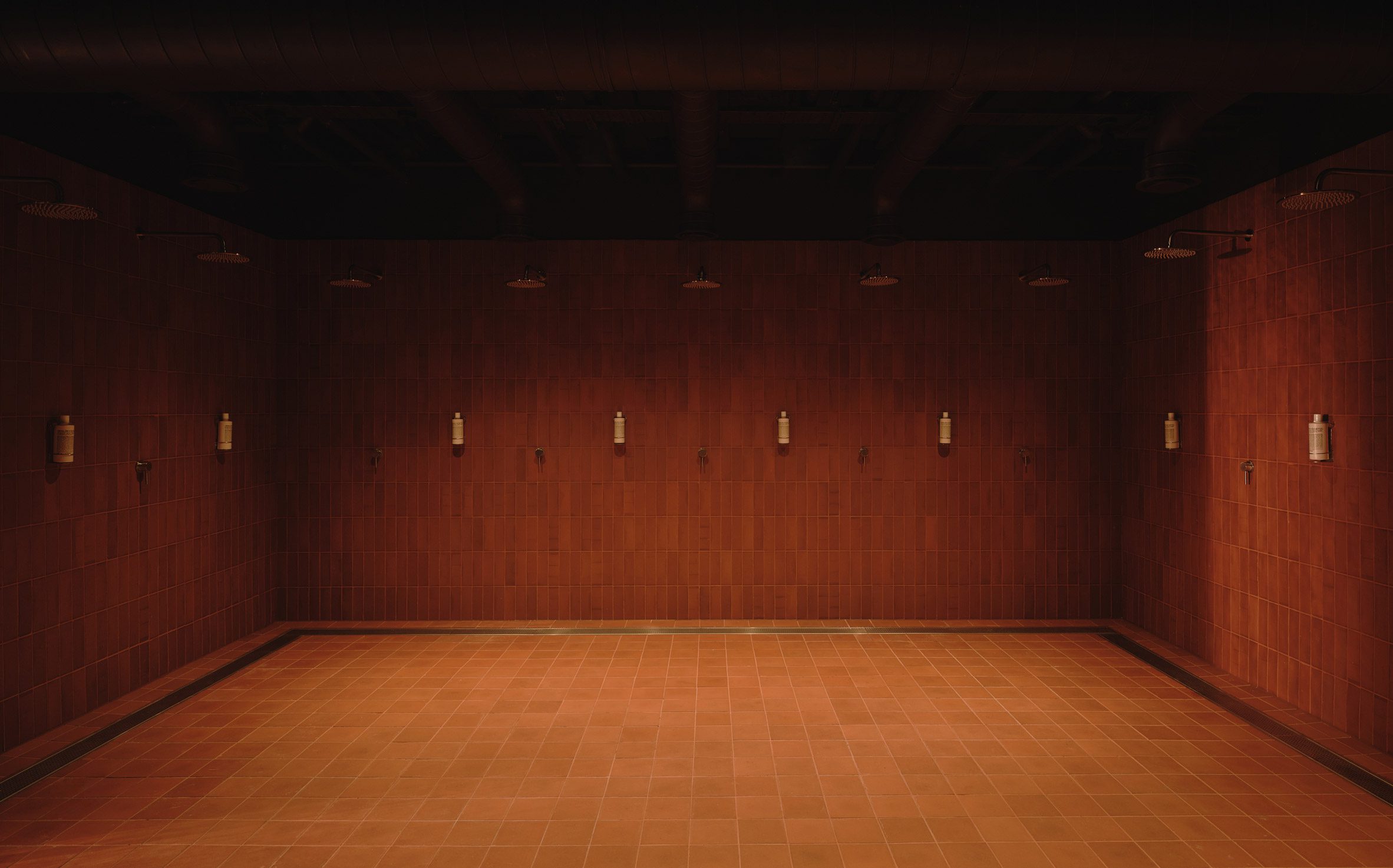 Arc Canary Wharf by Cake Architecture — A rhythmic composition of terracotta floor tiles laid in a radial grid pattern radiates toward a central void, establishing the amphitheatre-style gathering...