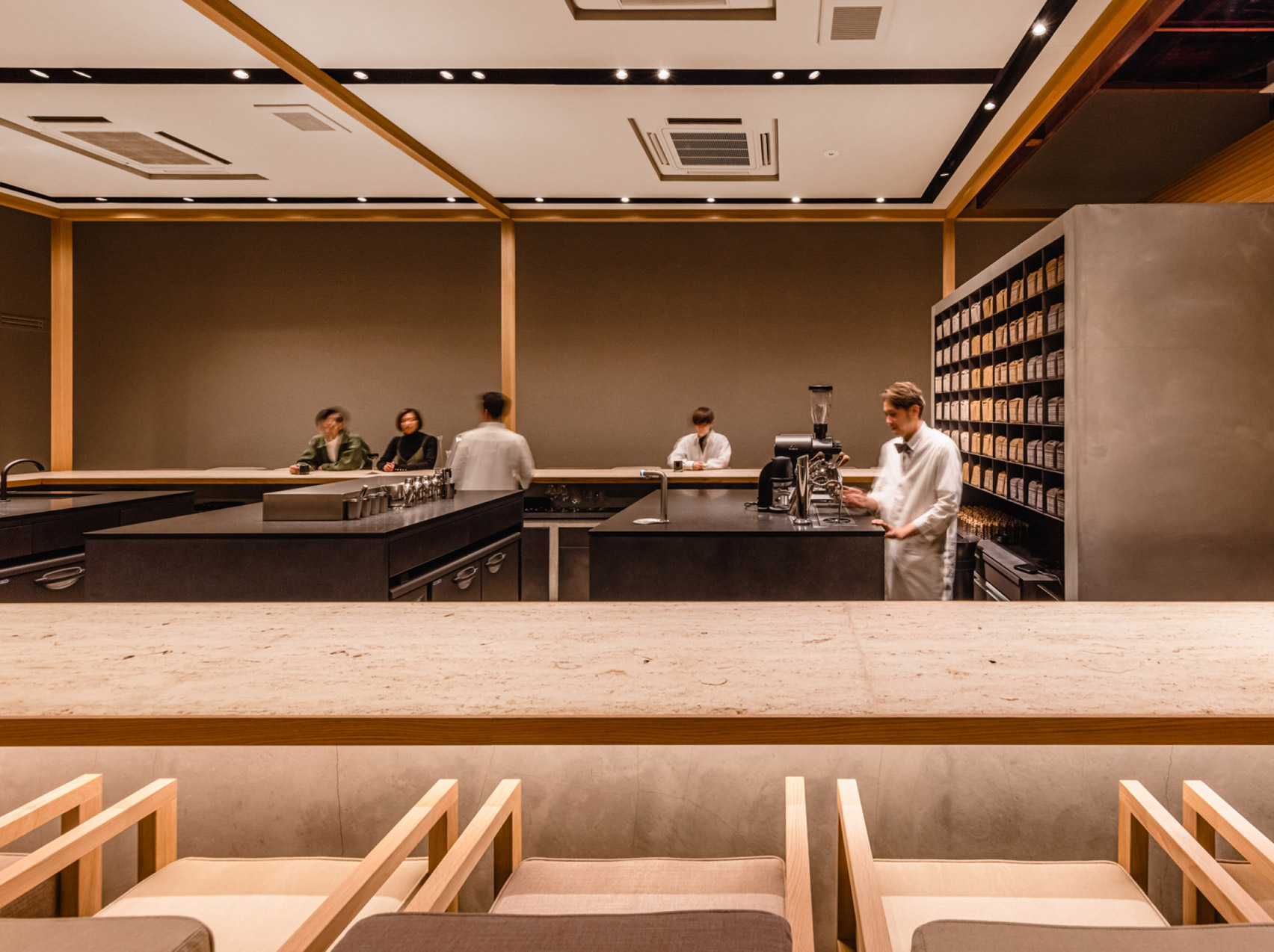 Koffee Mameya Kakeru by Fourteen Stones Design — Interior view of Koffee Mameya Kakeru shows the counter workspace elevated on a concrete platform, framed by timber-edged apertures in the foreground.