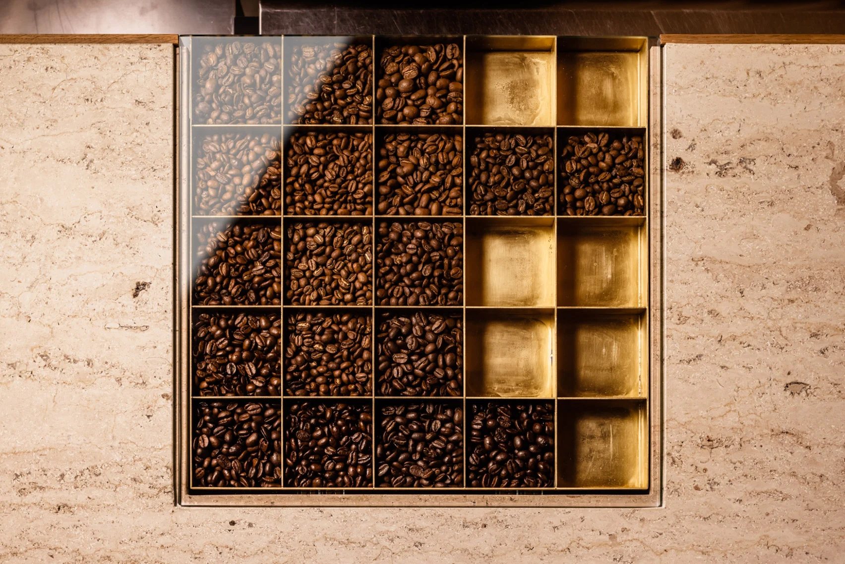 Koffee Mameya Kakeru by Fourteen Stones Design — A custom coffee bean display box mounted against a travertine wall creates a modular grid system.