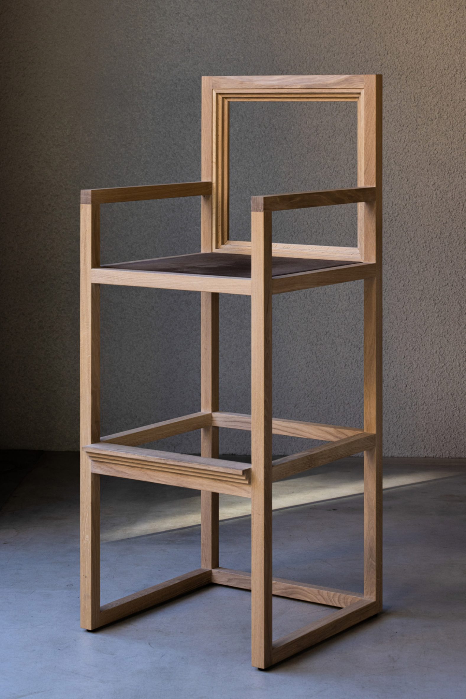 Koffee Mameya Kakeru by Fourteen Stones Design — A wooden chair frame photographed against a textured gray wall, showcasing joinery and construction details.