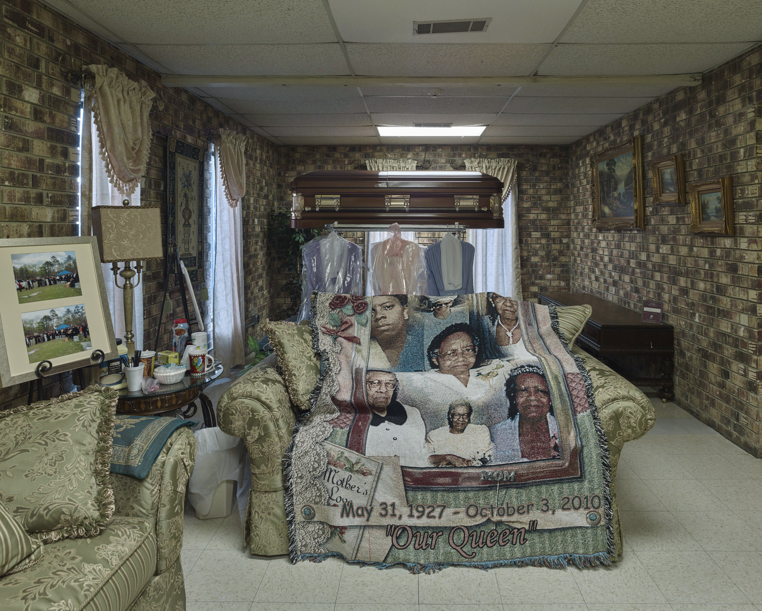 Funeral Homes of the American South by Timothy Hursley — A casket draped with a photo-printed textile memorial blanket dominates the center of this viewing room, positioned above a toy train track that circuits...