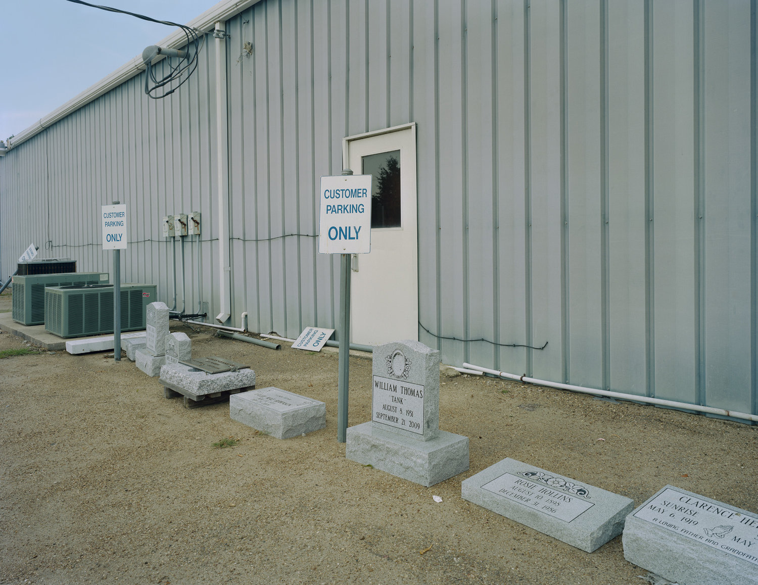 Funeral Homes of the American South by Timothy Hursley — A corrugated metal industrial building serves as an unexpected backdrop for a modest cemetery.