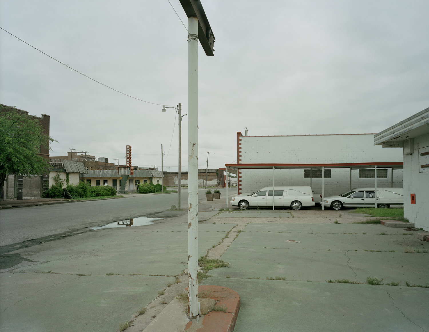 Funeral Homes of the American South by Timothy Hursley — A deteriorating rural commercial street corner in the American South, centered on a white utility pole with utility lines extending across the frame.