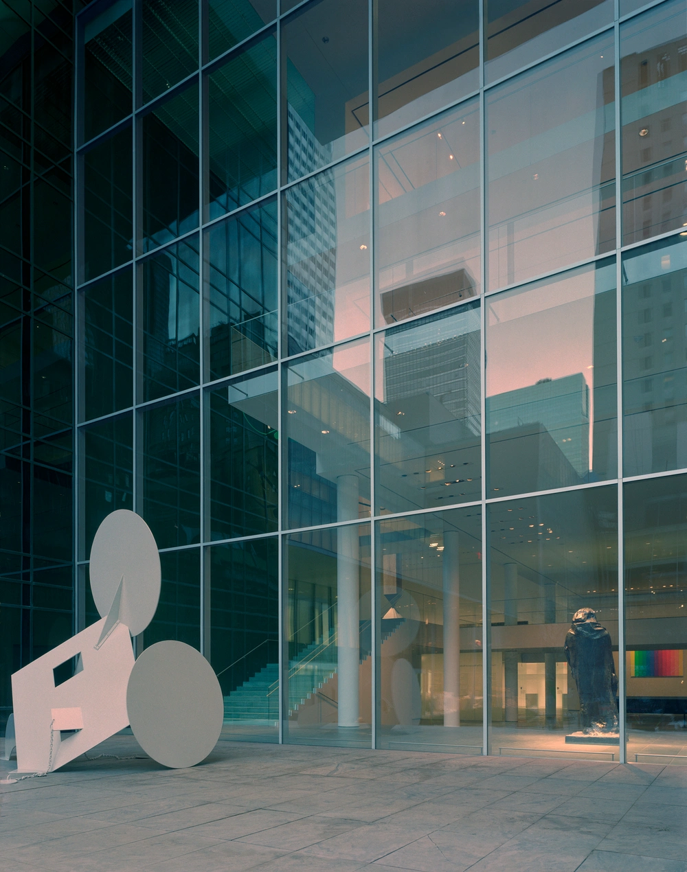 Museum of Modern Art in New York by Yoshio Taniguchi — A white sculptural element occupies the plaza threshold of MoMA's glass curtain wall, its geometric form—composed of circular and angular...