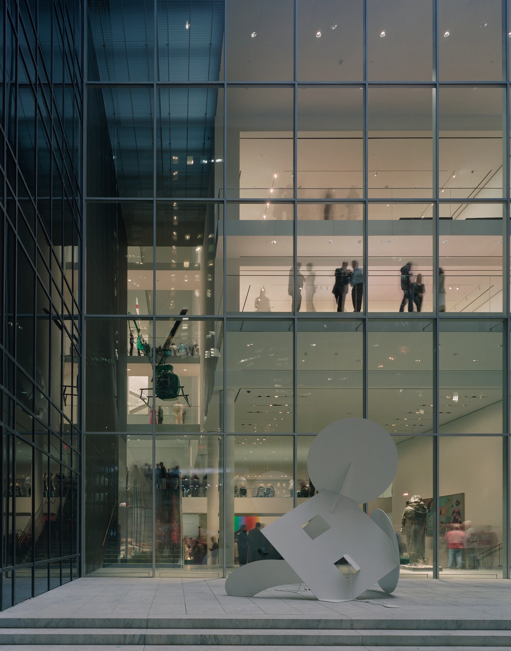 Museum of Modern Art in New York by Yoshio Taniguchi — A white sculptural form occupies the plaza threshold before MoMA's glass curtain wall, its geometric cutouts and tilted orientation creating visual contrast...