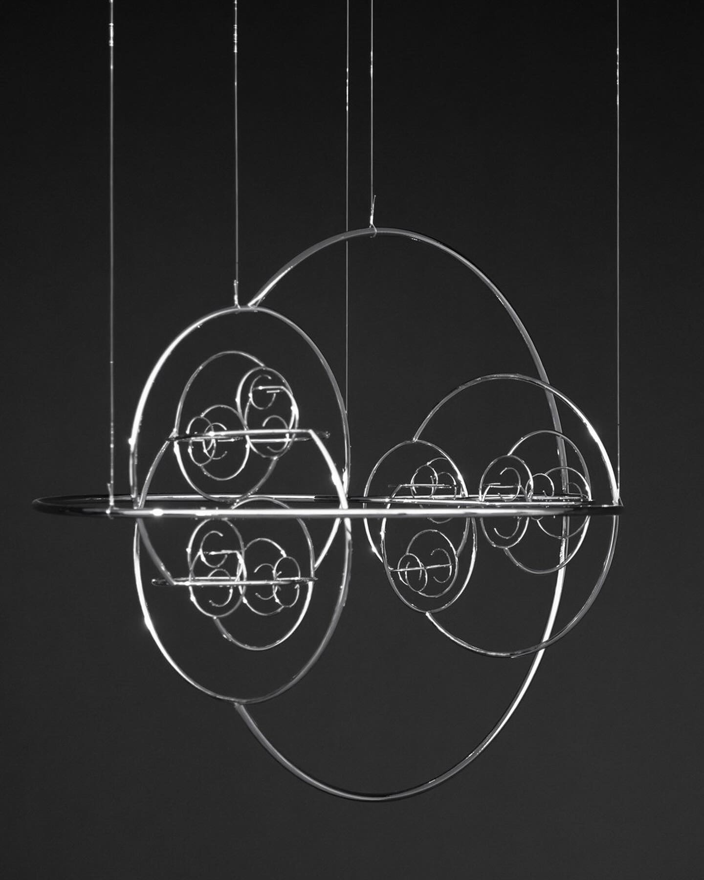 Many Worlds Over by Ayoung Kim at Hamburger Bahnhof — A kinetic sculpture suspended against black void, composed of nested steel rings and circular forms arranged in graduated sizes along a horizontal axis.