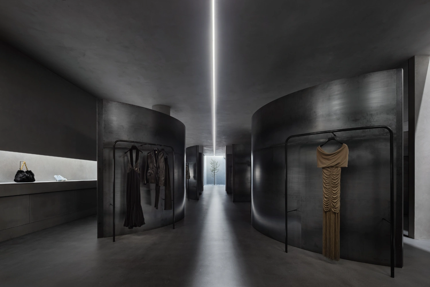 KHAITE Flagship Store by Griffin Frazen — The KHAITE flagship store interior presents a sectioned retail environment defined by curved dark steel partition walls that create sequential display chambers.