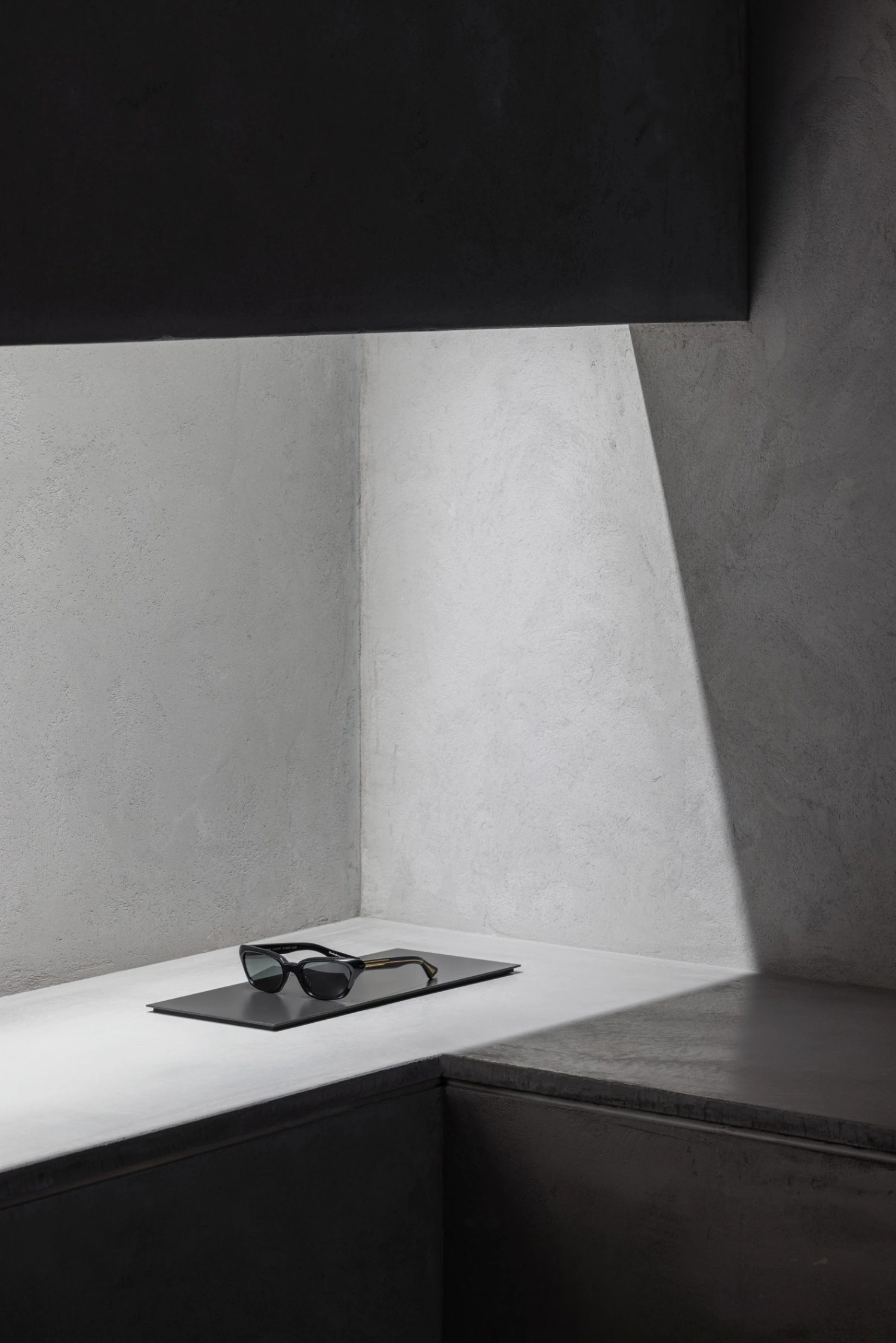 KHAITE Flagship Store by Griffin Frazen — A minimalist interior corner captured in sharp detail, where monolithic concrete walls meet in a right angle beneath a dark overhead plane.