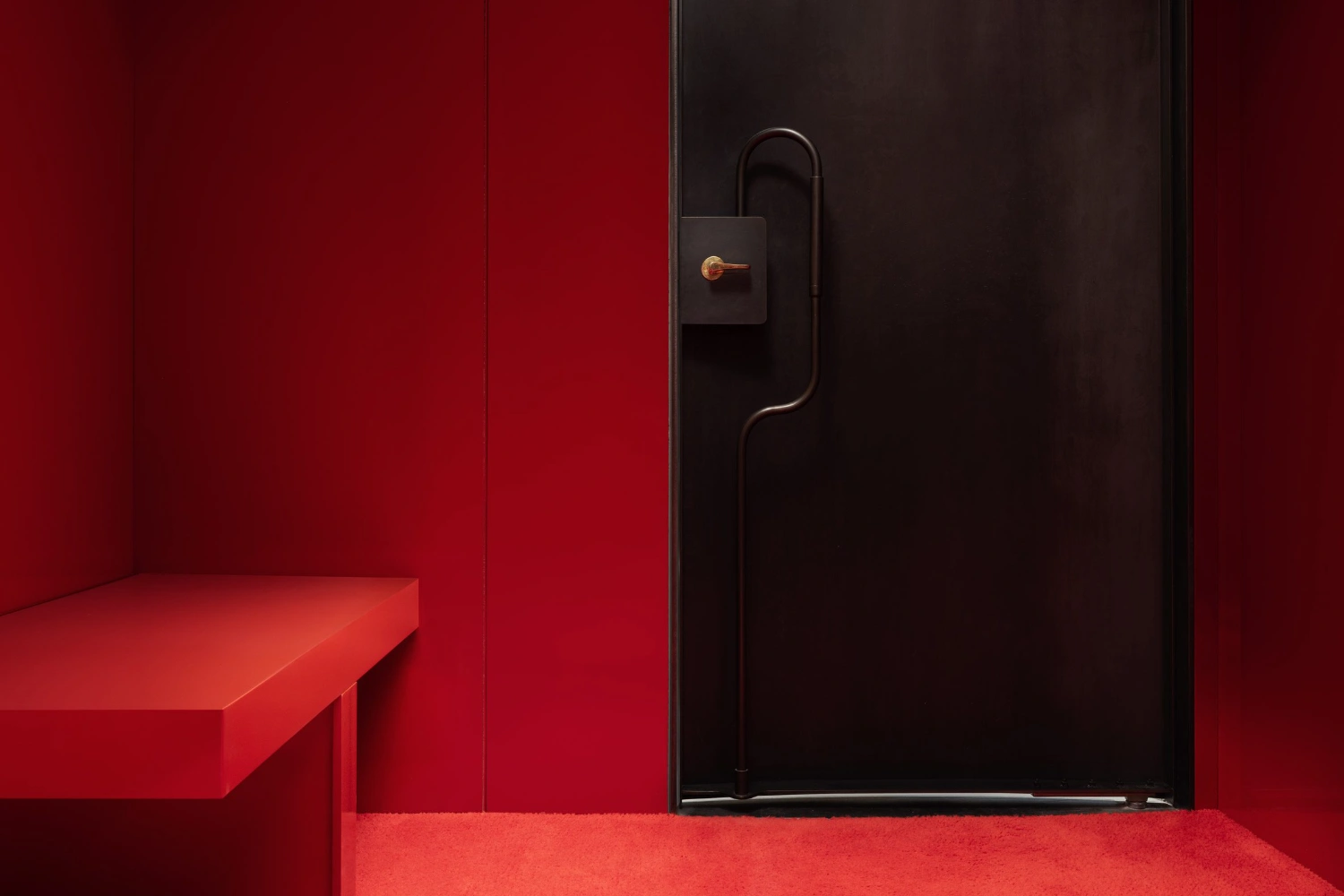 KHAITE Flagship Store by Griffin Frazen — A contained passage defined by monolithic crimson walls and a black steel partition, creating a compressed threshold within the KHAITE flagship store.