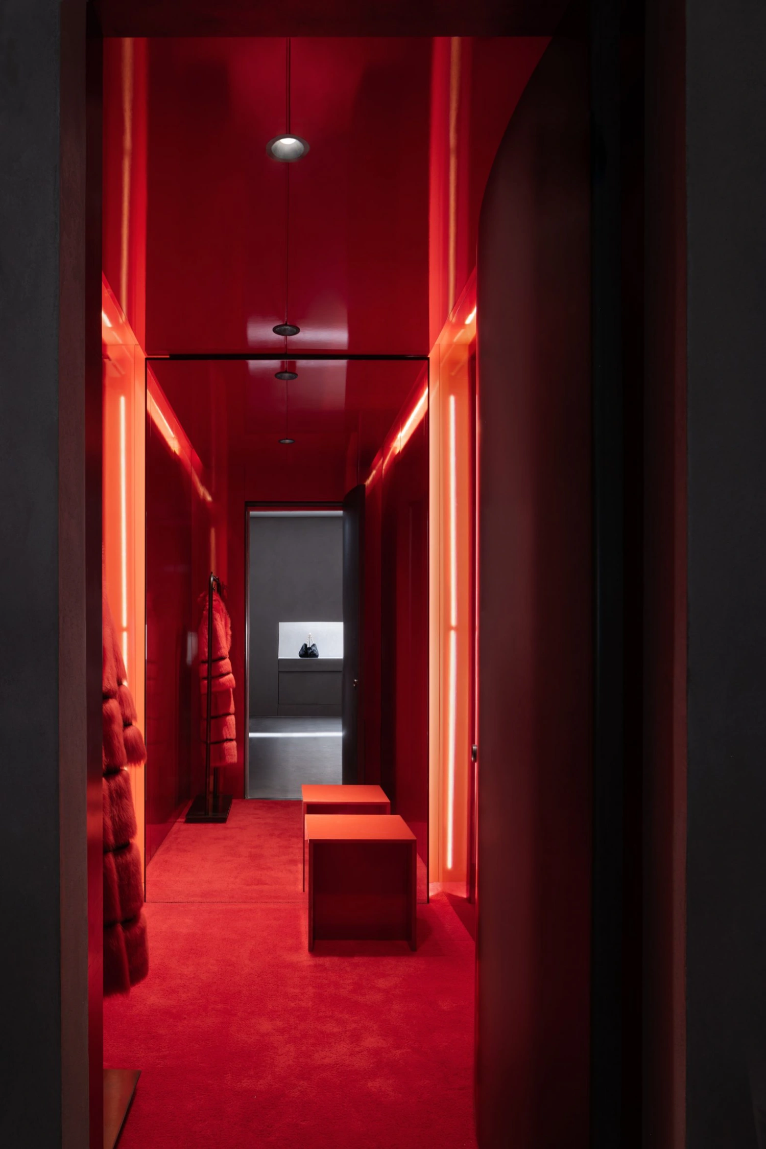 KHAITE Flagship Store by Griffin Frazen — A narrow corridor lined with vivid red walls and neon tube lighting that traces the perimeter in sharp orange-red lines.