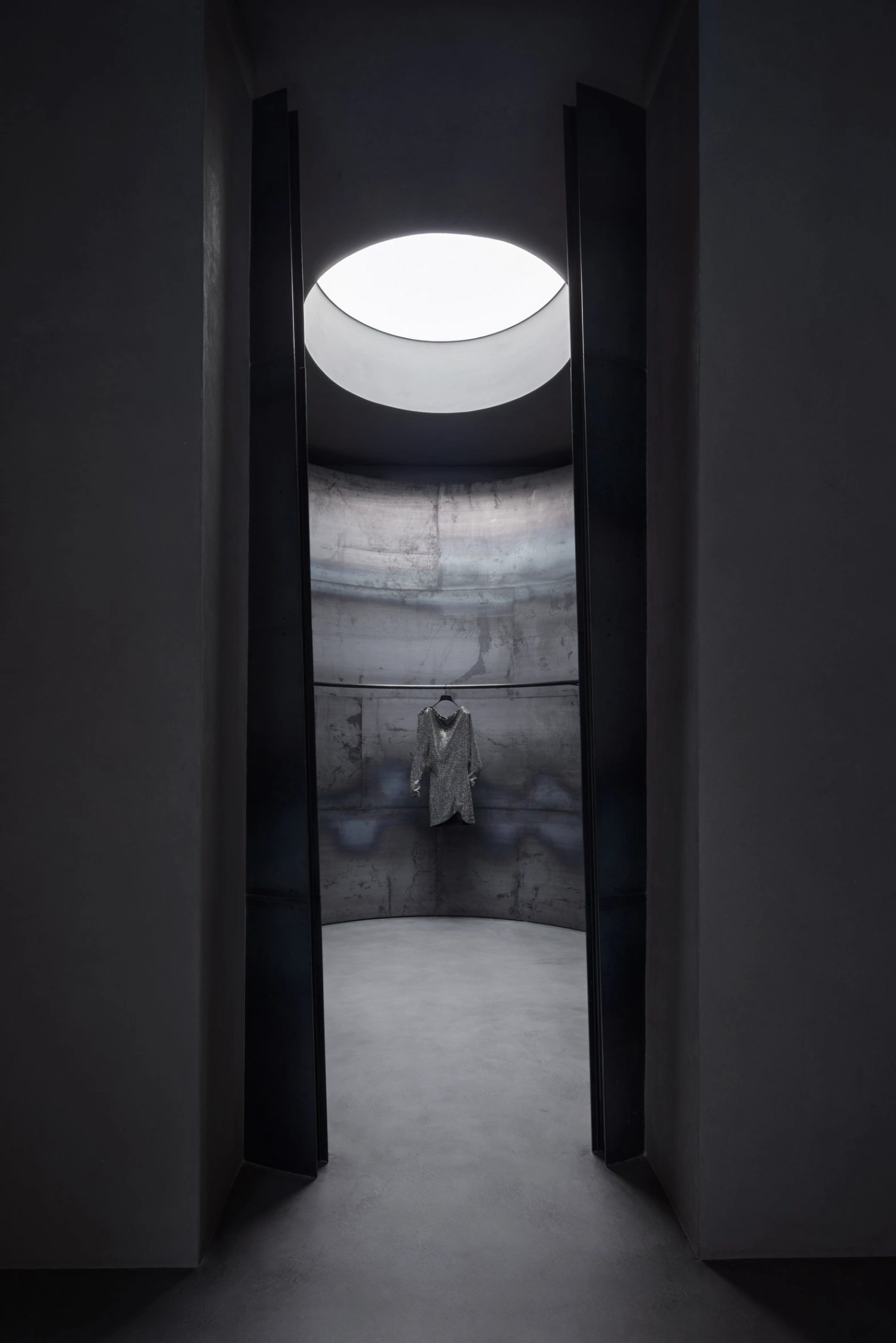 KHAITE Flagship Store by Griffin Frazen — A narrow corridor framed by two vertical dark steel partitions converges toward a distant chamber.