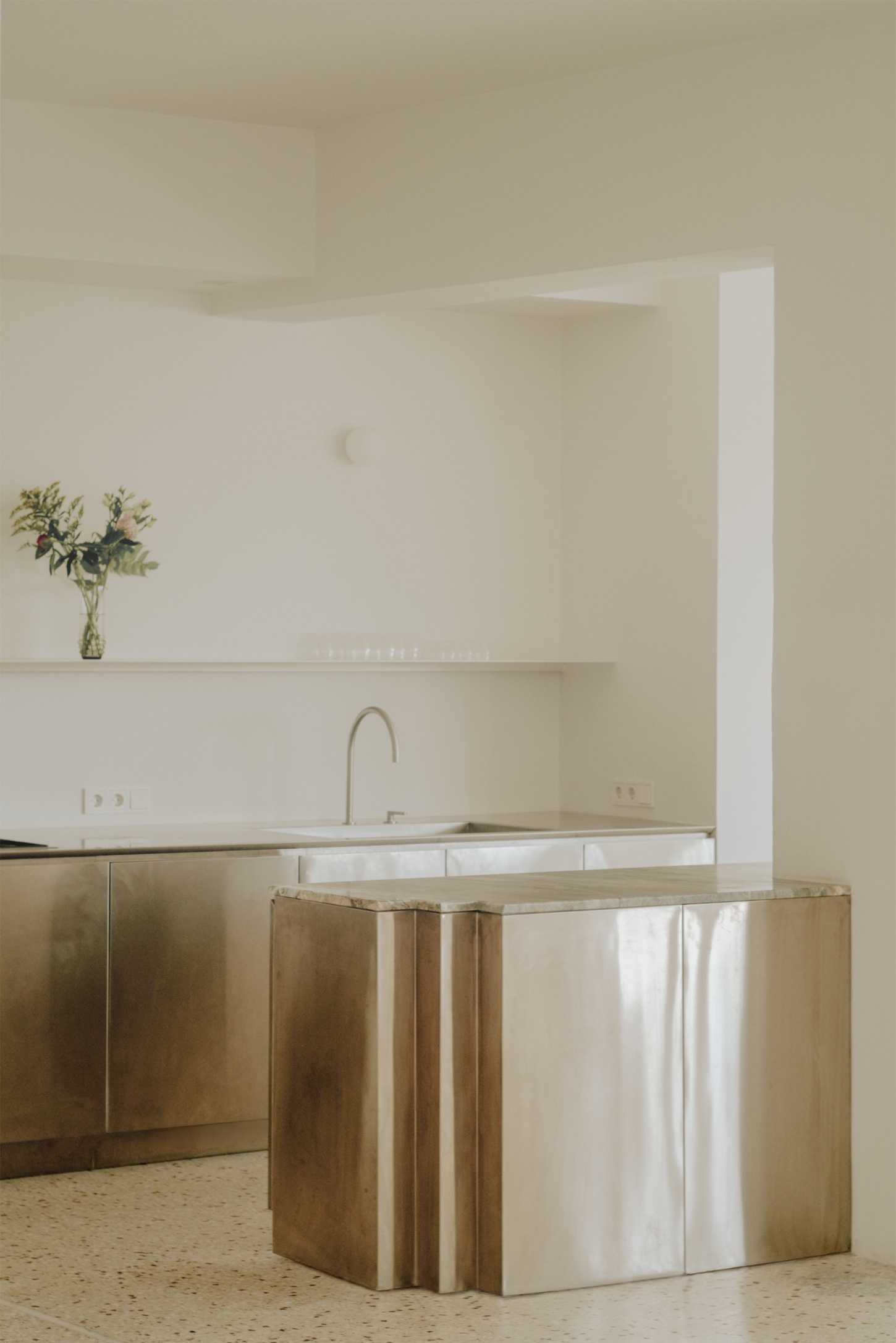 'Astral Weeks' by Oblique — A kitchen island clad in brushed brass and white fabric wraps around a load-bearing column, transforming structural necessity into sculptural form.