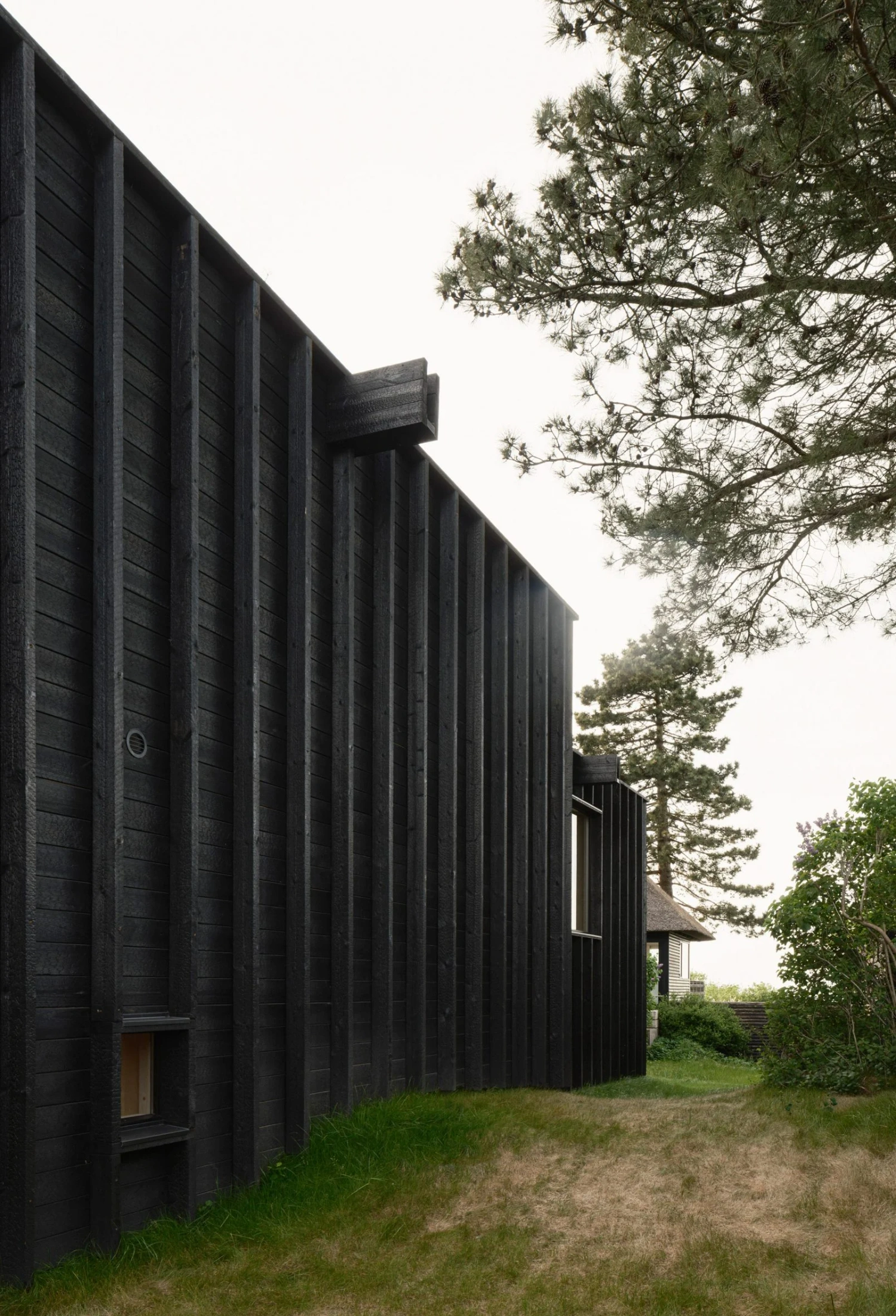 House with a Hidden Atrium by Förstberg Ling — The blackened pine facade dominates the frame, its vertical timber ribs casting deep shadow lines across the weathered surface.