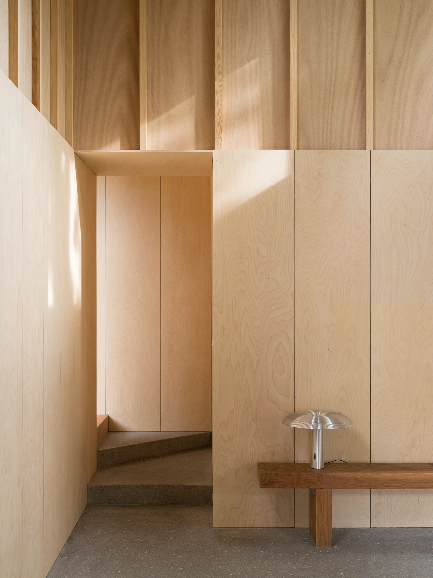 House with a Hidden Atrium by Förstberg Ling — Interior passage lined with light timber paneling in vertical boards, creating rhythmic shadow lines across walls and ceiling.