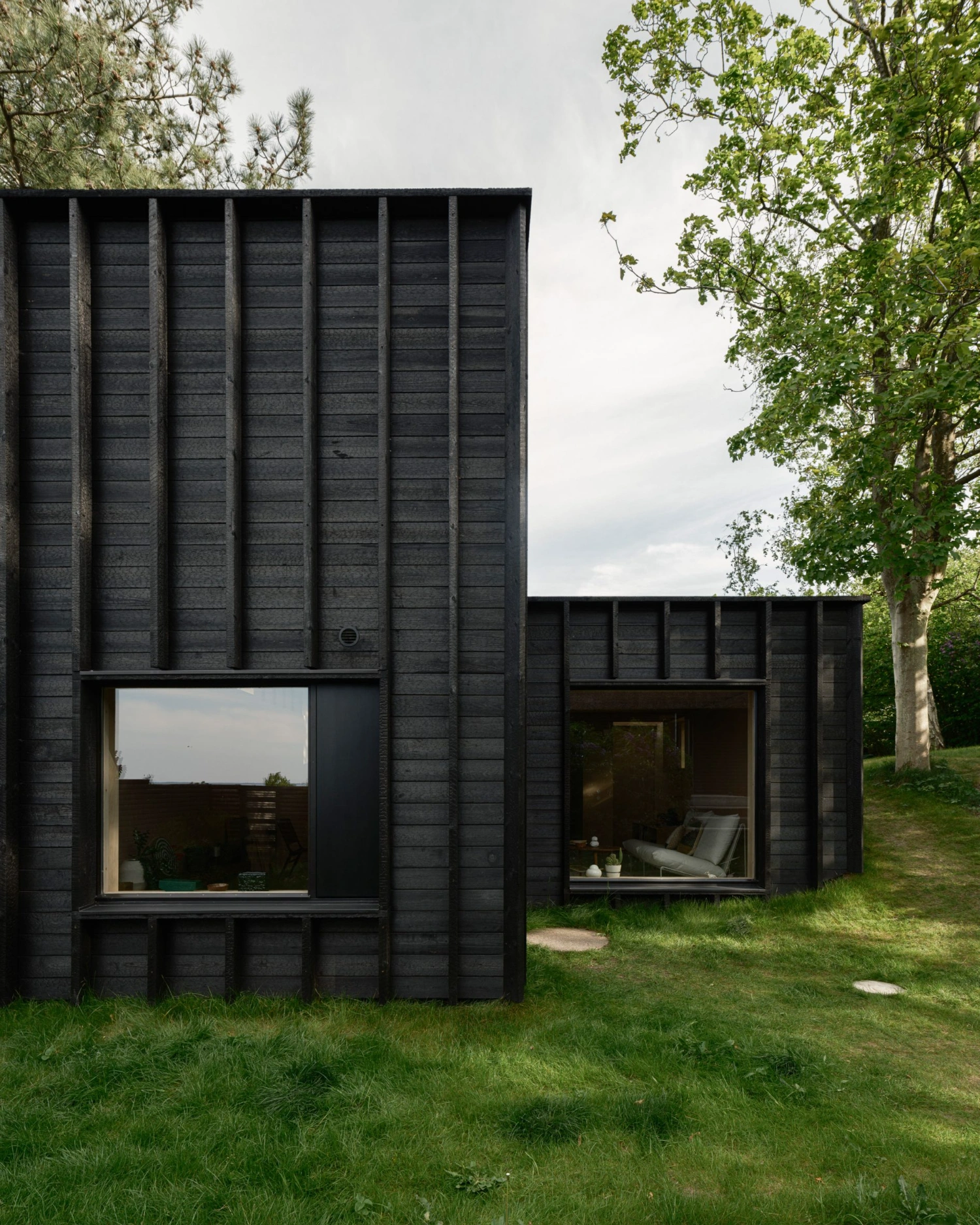 House with a Hidden Atrium by Förstberg Ling — The blackened pine facade presents a rhythmic composition of seven vertical timber ribs that cast deep shadow lines across the elevation.