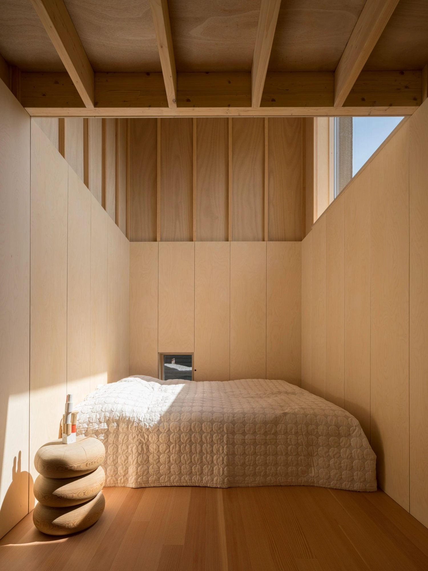 House with a Hidden Atrium by Förstberg Ling — A bedroom enclosed by floor-to-ceiling timber paneling in warm honey tones, with vertical board-and-batten wall treatment creating subtle shadow striations.