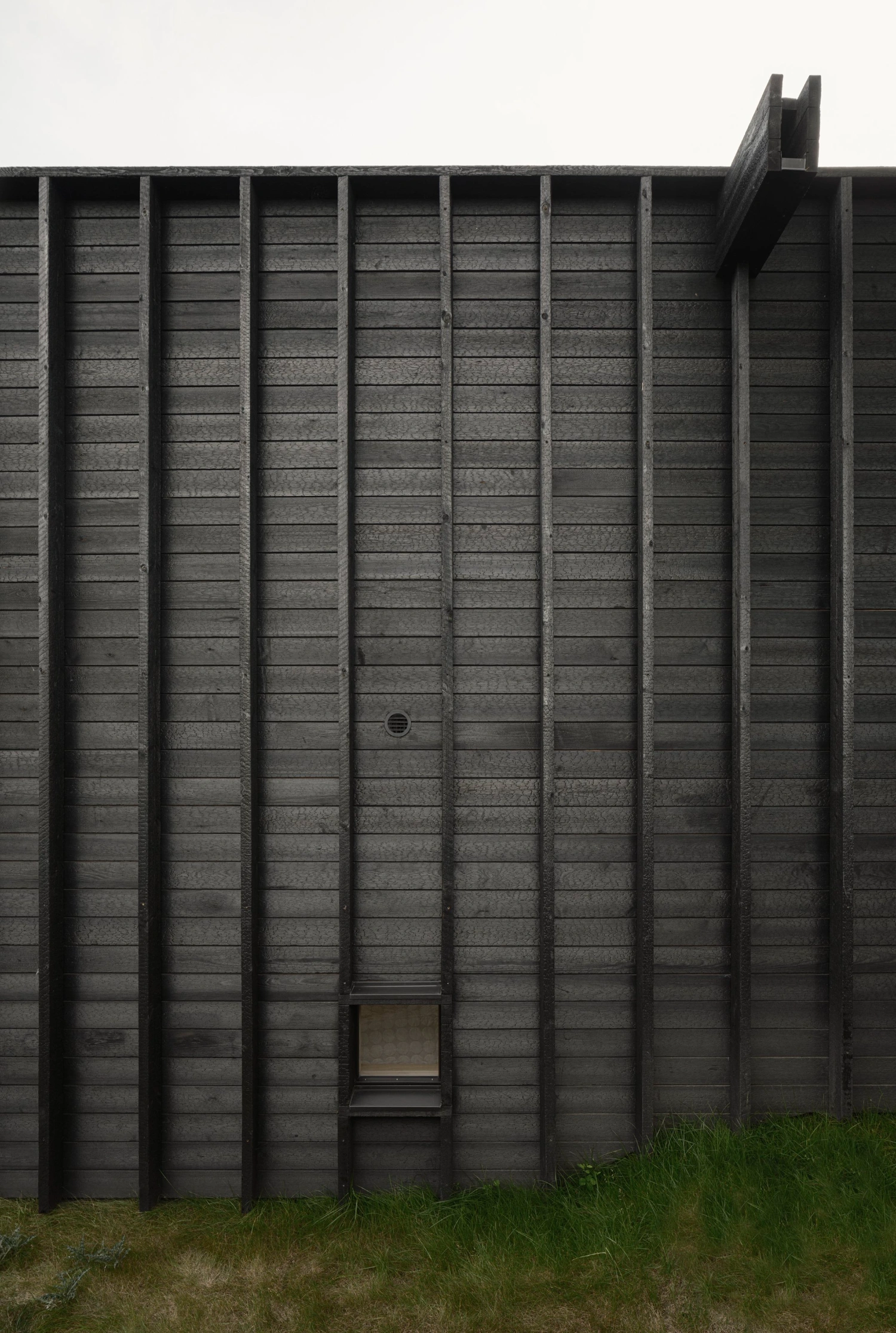 House with a Hidden Atrium by Förstberg Ling — The blackened pine facade presents a rhythmic composition of vertical timber ribs that cast deep shadow lines across the board-formed cladding.