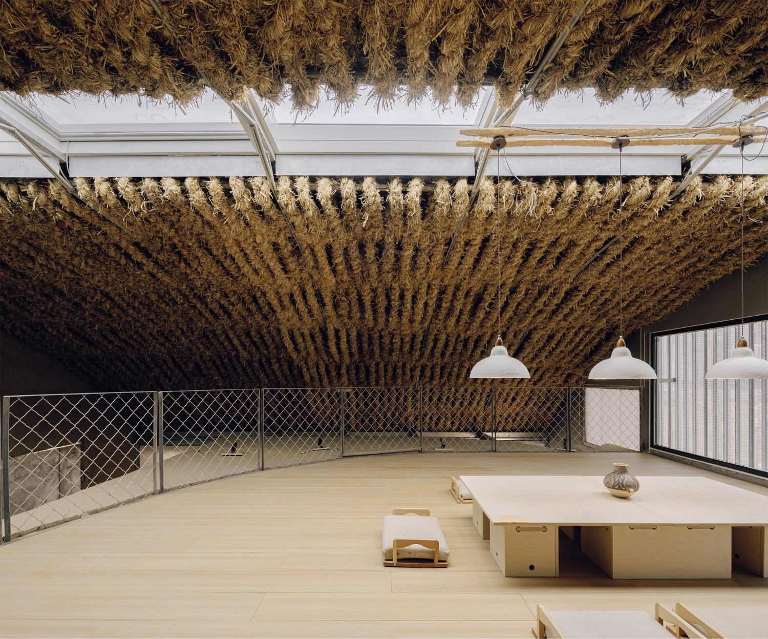 Home in the Badain Jaran Desert by School of Architecture and Urban Planning NJU — A cavernous interior dominated by suspended bundles of dried straw and reed harvested from local wetlands, creating a textured ceiling plane that responds...