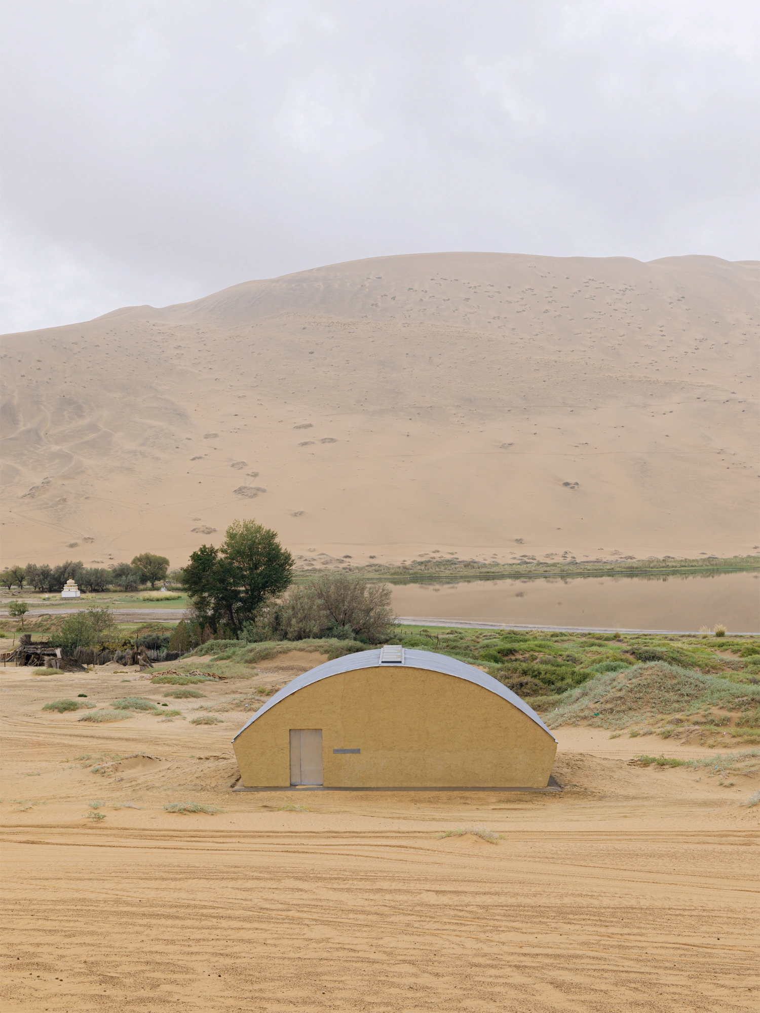 Home in the Badain Jaran Desert by School of Architecture and Urban Planning NJU — A half-cylindrical structure with rendered earthen walls sits embedded in the desert floor, its arched profile echoing the dunes beyond.