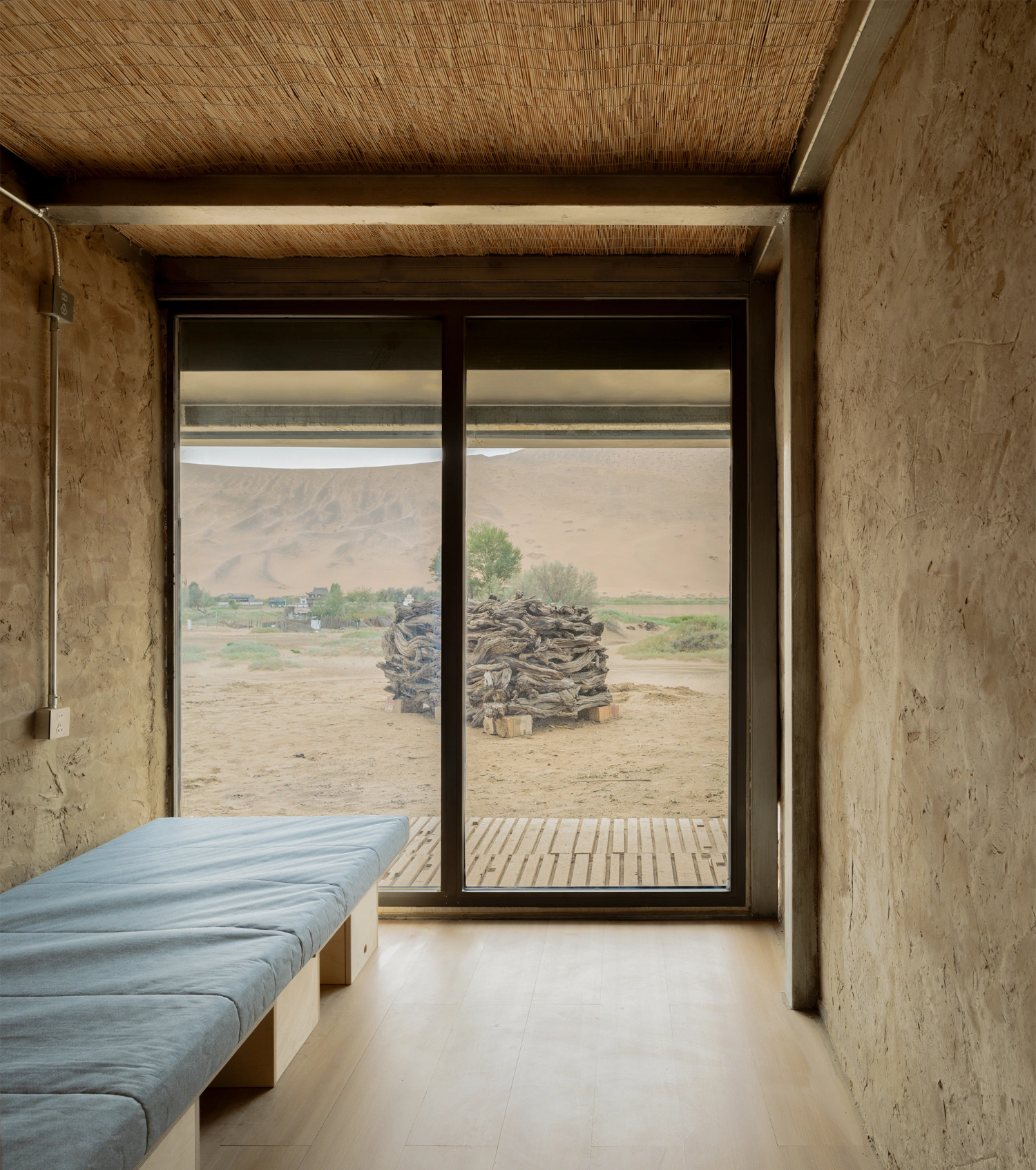 Home in the Badain Jaran Desert by School of Architecture and Urban Planning NJU — A minimalist bedroom interior frames the desert landscape through floor-to-ceiling sliding glass doors.