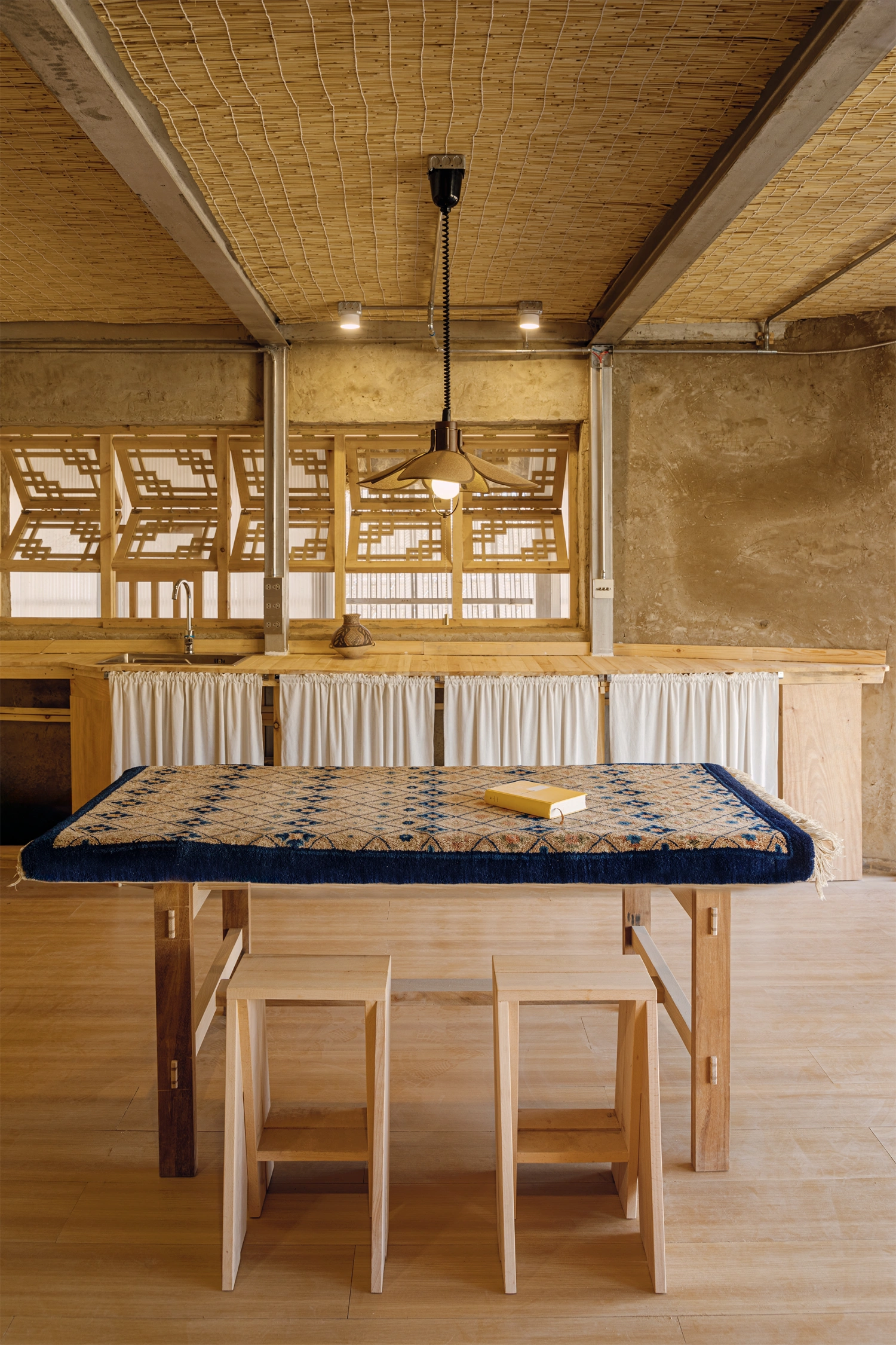 Home in the Badain Jaran Desert by School of Architecture and Urban Planning NJU — Interior view of a central communal space anchored by a monolithic timber table with integrated storage compartments and wooden handles.