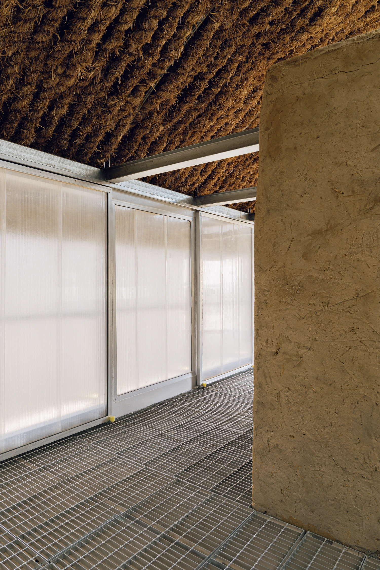 Home in the Badain Jaran Desert by School of Architecture and Urban Planning NJU — A passage framed by a monolithic rammed-earth wall on the right, its surface marked by visible striations and trowel marks.