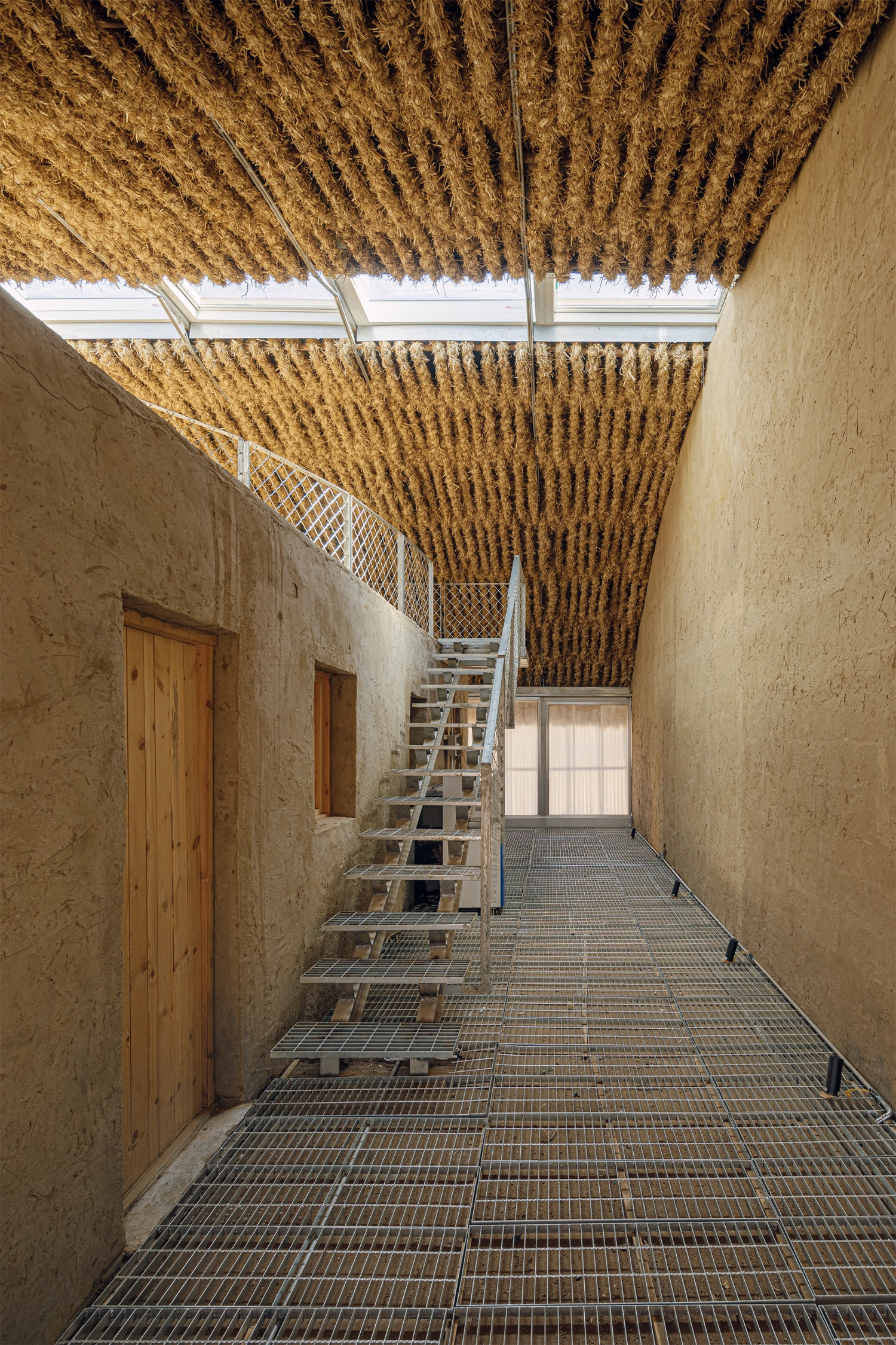 Home in the Badain Jaran Desert by School of Architecture and Urban Planning NJU — A linear passage anchors the project's interior organization, its corrugated metal flooring creating rhythmic shadow patterns beneath a dramatic overhead...