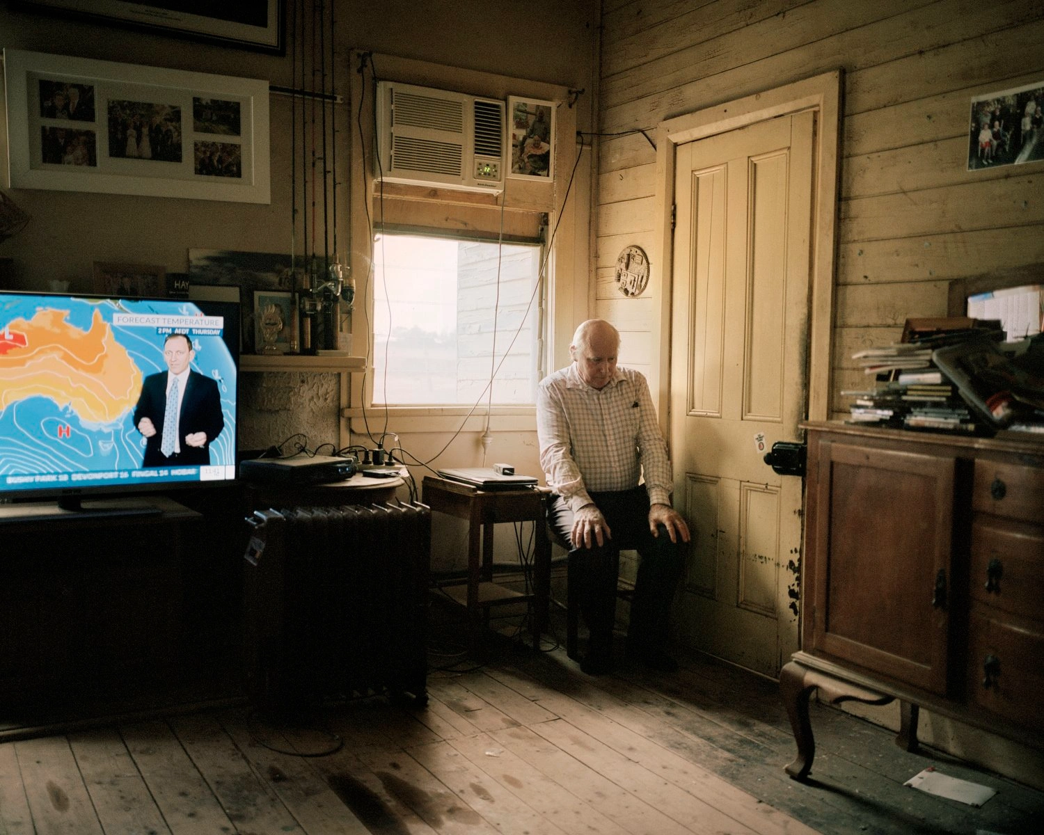 Big Sky by Adam Ferguson — A man in a cream linen shirt sits centrally within a timber-lined interior, his posture slumped and contemplative.