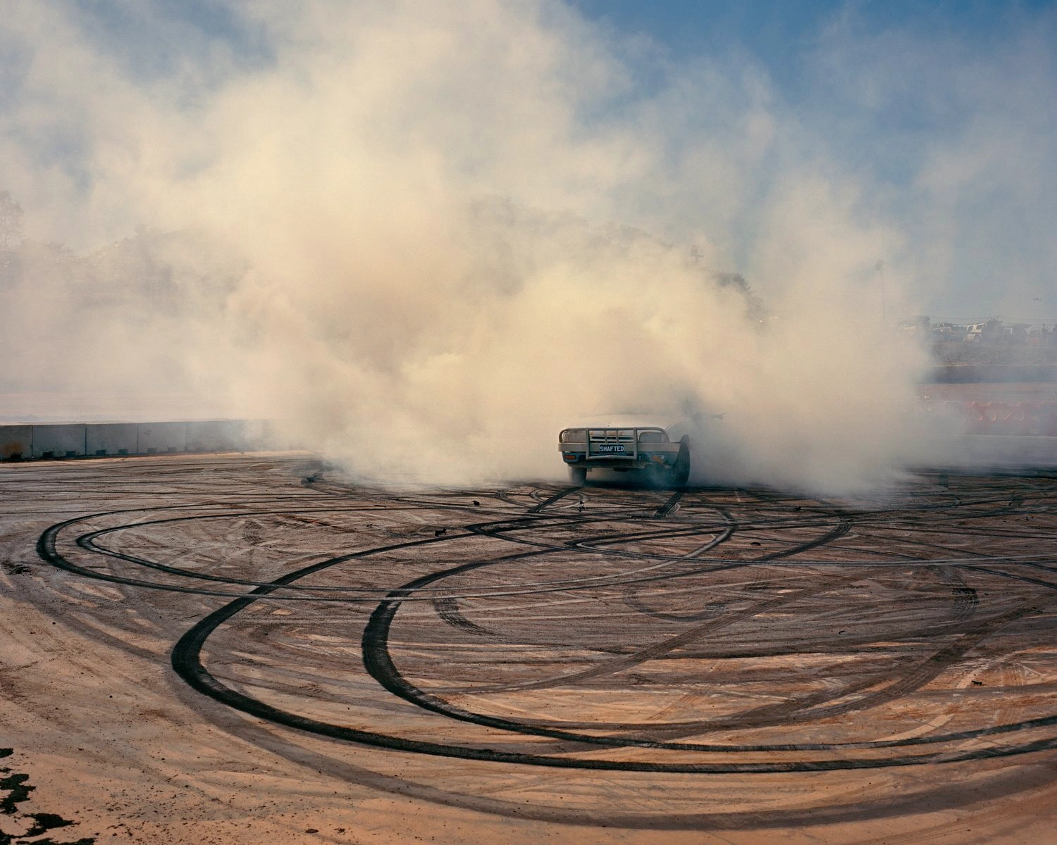 Big Sky by Adam Ferguson — A GMC truck executes a controlled skid across bare earth, rear wheels locked and smoking heavily in a billowing cloud of dust and tire smoke.