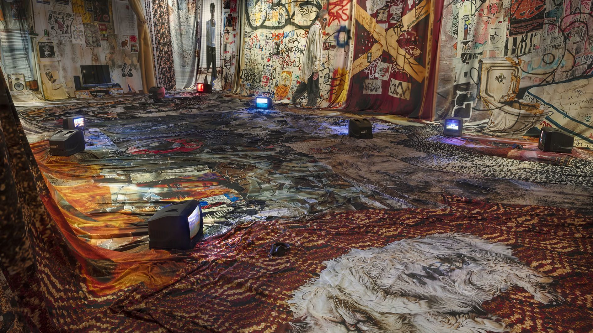 Proof of Concept by Jon Rafman at Sprüth Magers LA — The gallery floor is densely layered with patterned textiles in rust, ochre, and burgundy tones, creating a maximalist foundation for the exhibition.