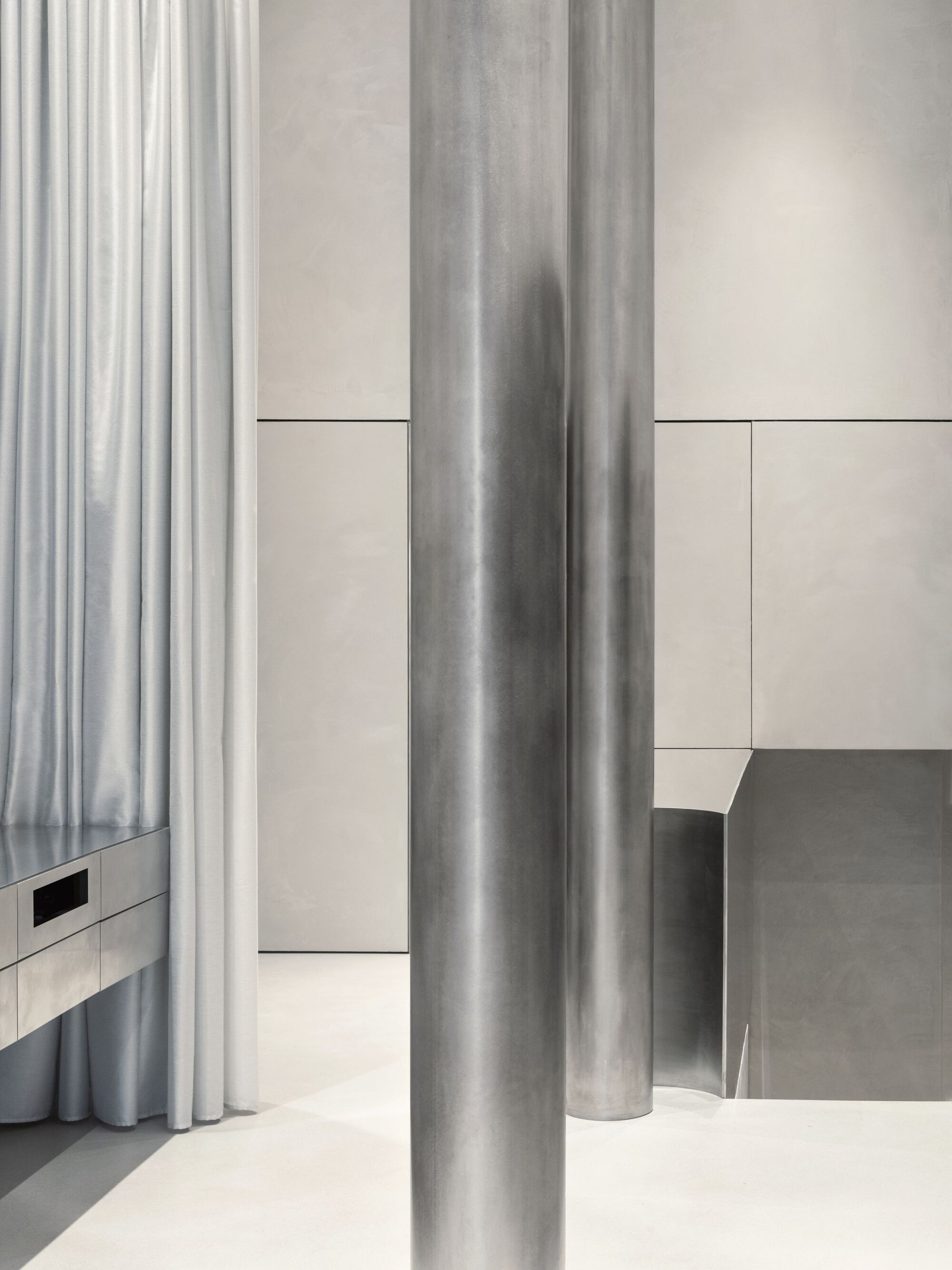 Aesop Store Barcelona by BAROZZI VEIGA — Interior passage defined by cylindrical metal columns in brushed steel, their reflective surfaces catching lateral light.