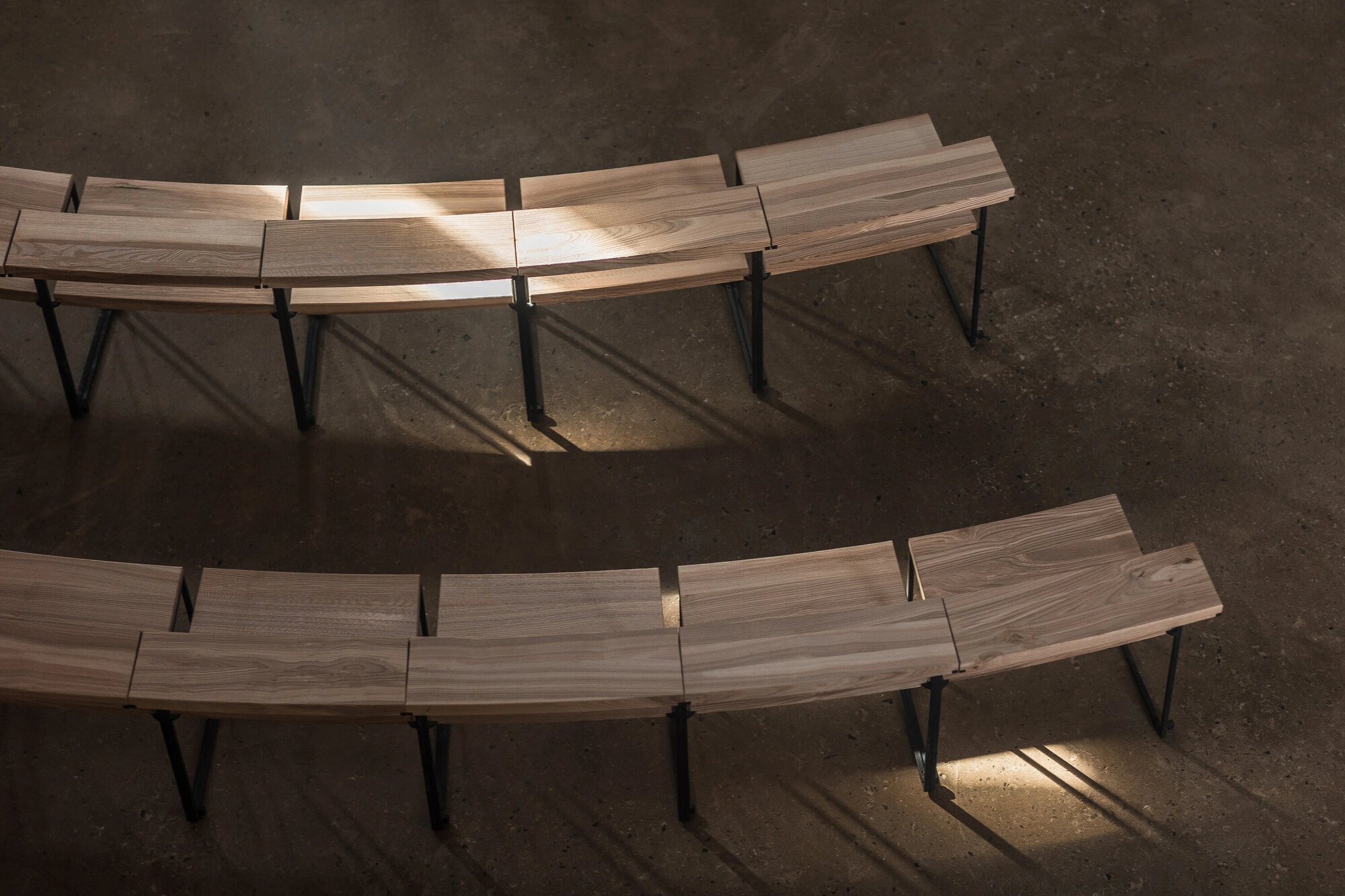 Our Lady of Sorrows Chapel by RCNKSK — Overhead perspective of the chapel's interior seating arrangement, revealing two curved rows of timber benches with metal-frame supports positioned on...