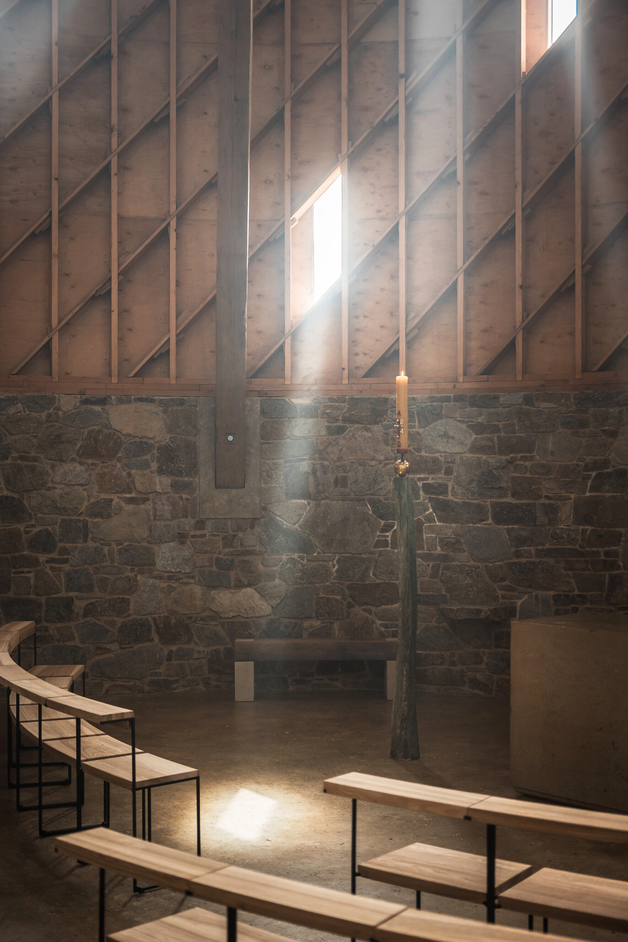 Our Lady of Sorrows Chapel by RCNKSK — The chapel interior is illuminated by a single rectangular skylight, casting a sharp geometric beam across the timber-framed ceiling and down the central...