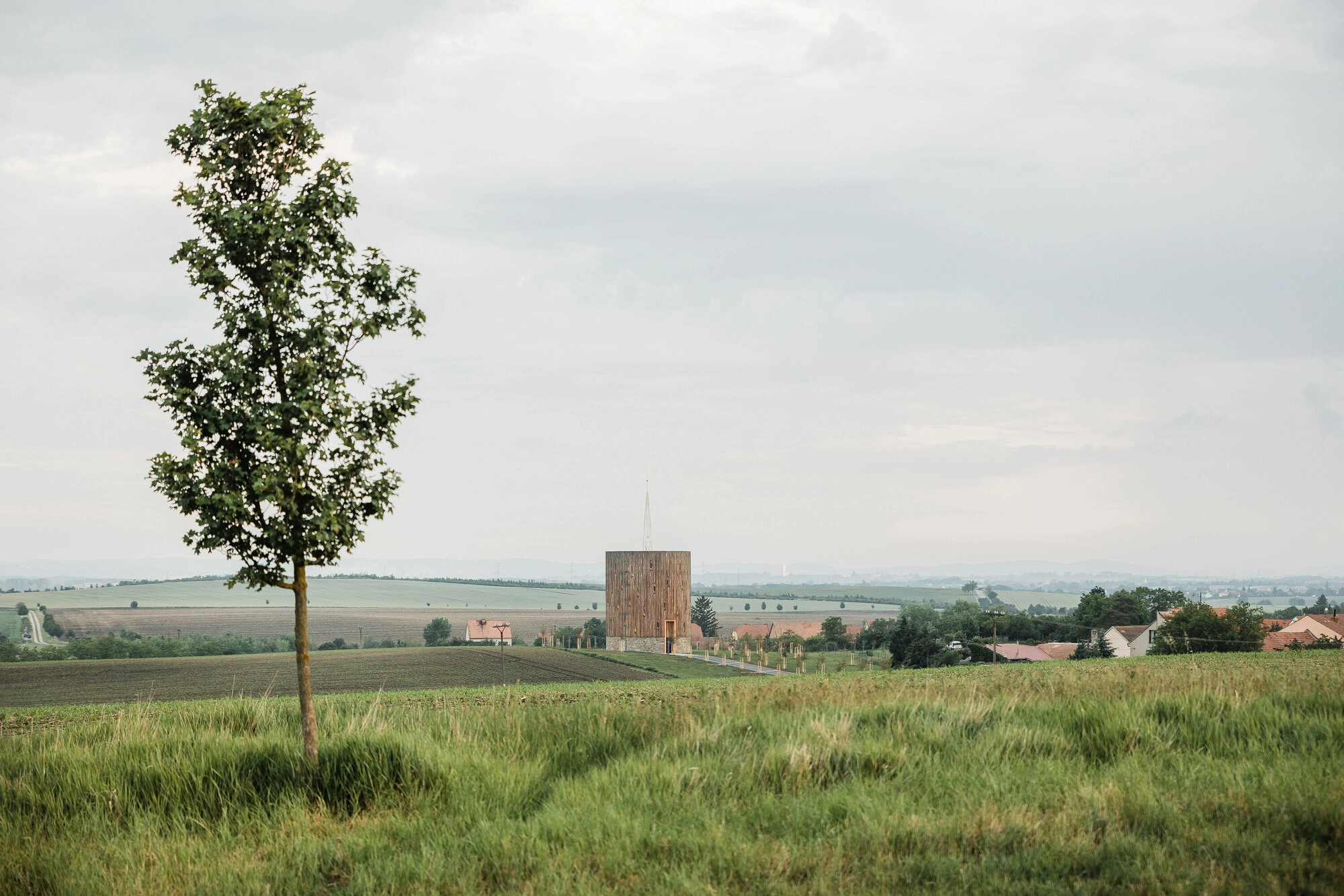 Our Lady of Sorrows Chapel by RCNKSK — The Our Lady of Sorrows Chapel emerges from flat agricultural land as a singular timber-clad volume, its wooden facade organized by seven ascending vertical...
