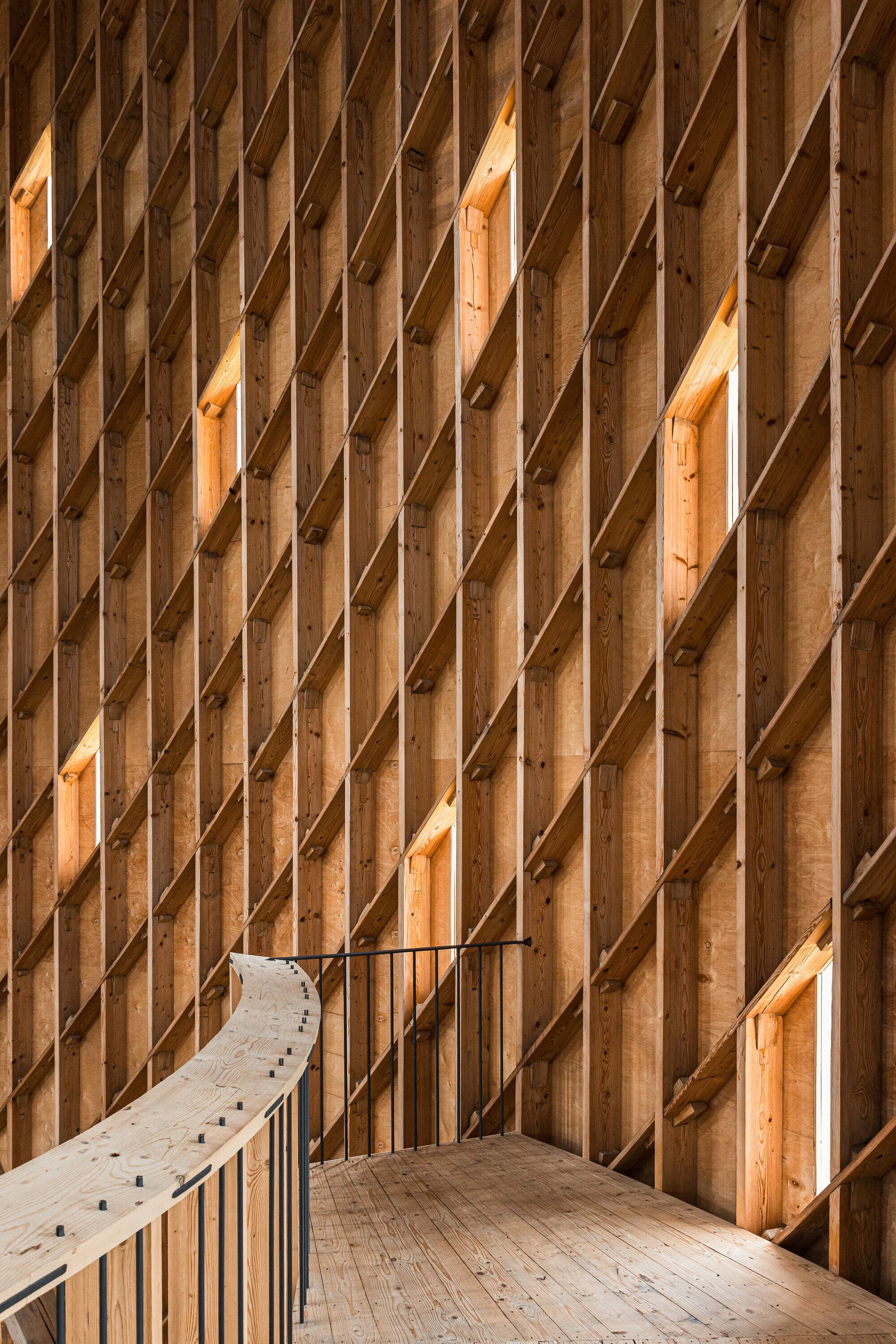 Our Lady of Sorrows Chapel by RCNKSK — Interior passage framed by repetitive timber vertical members in post-and-beam construction.