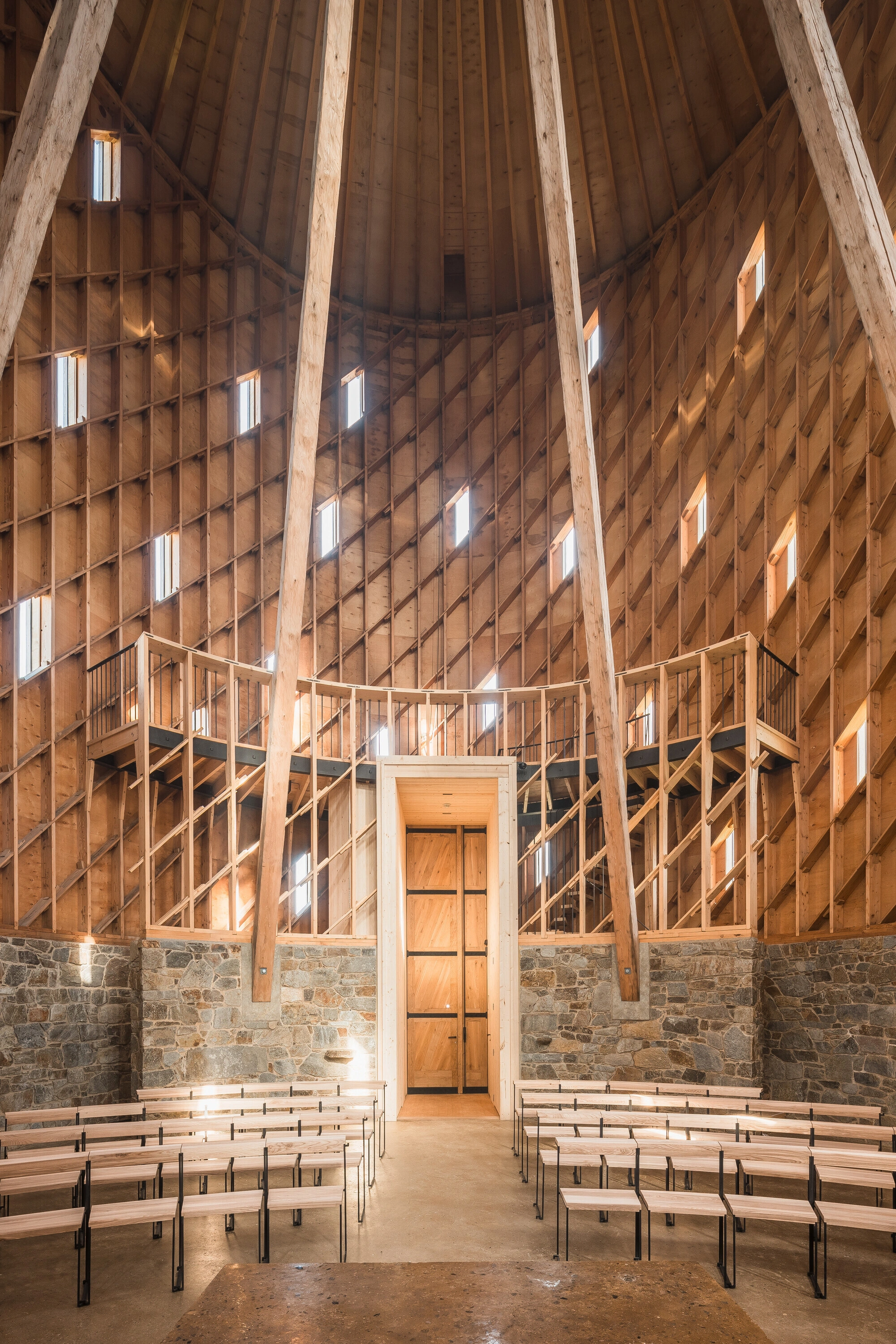 Our Lady of Sorrows Chapel by RCNKSK — Interior view of the chapel captured from the entrance threshold, revealing the radial timber roof structure converging toward the apex.