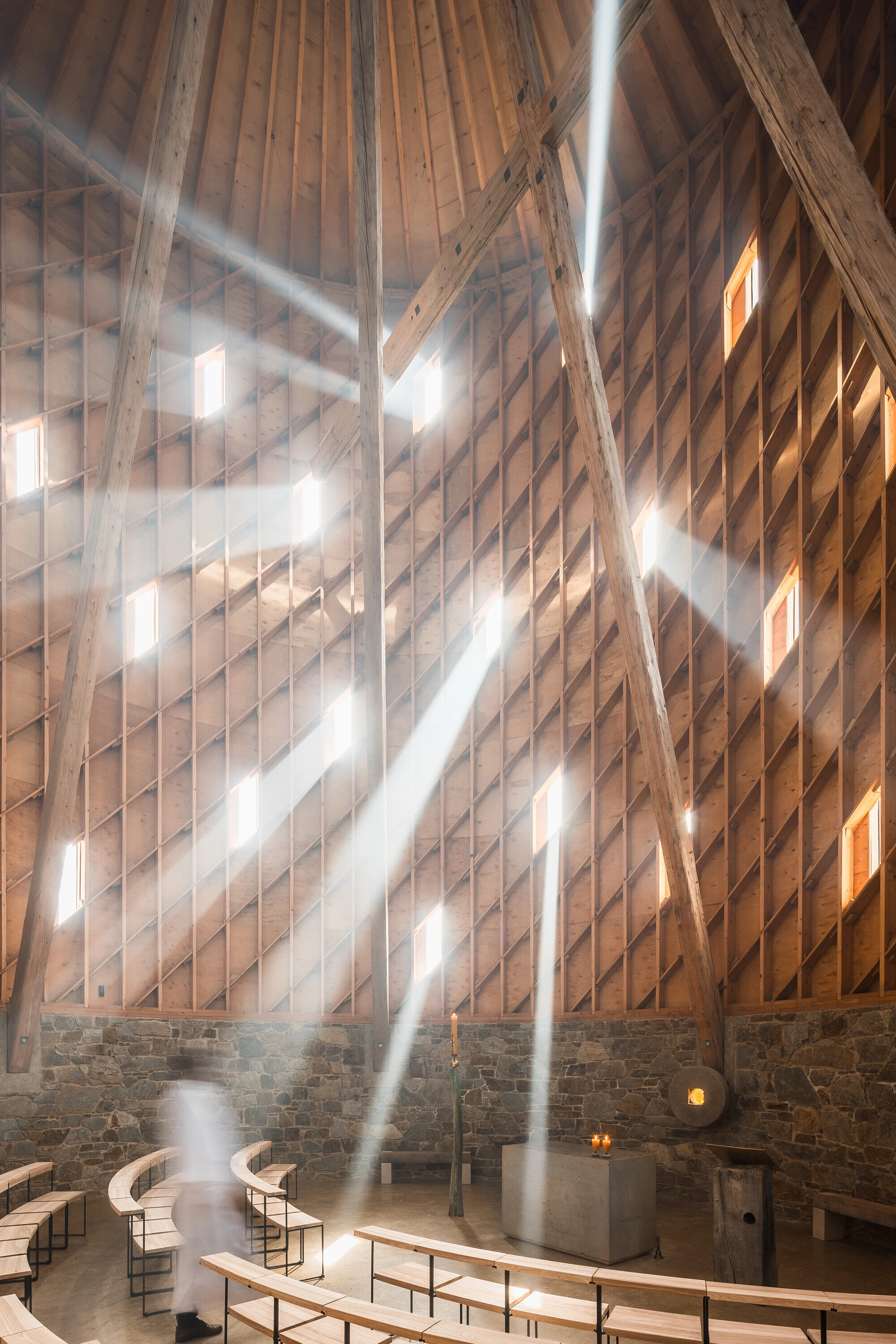 Our Lady of Sorrows Chapel by RCNKSK — Volumetric timber post-and-beam interior flooded with directional light through rectangular window openings.